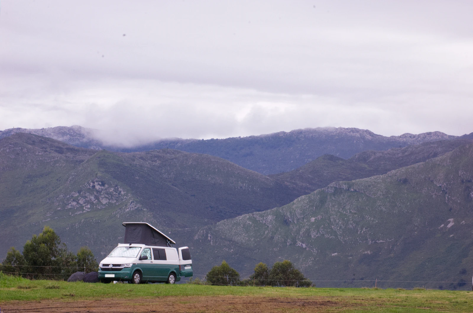Campervan parked on a grassy hill, mountains beyond, Asturias