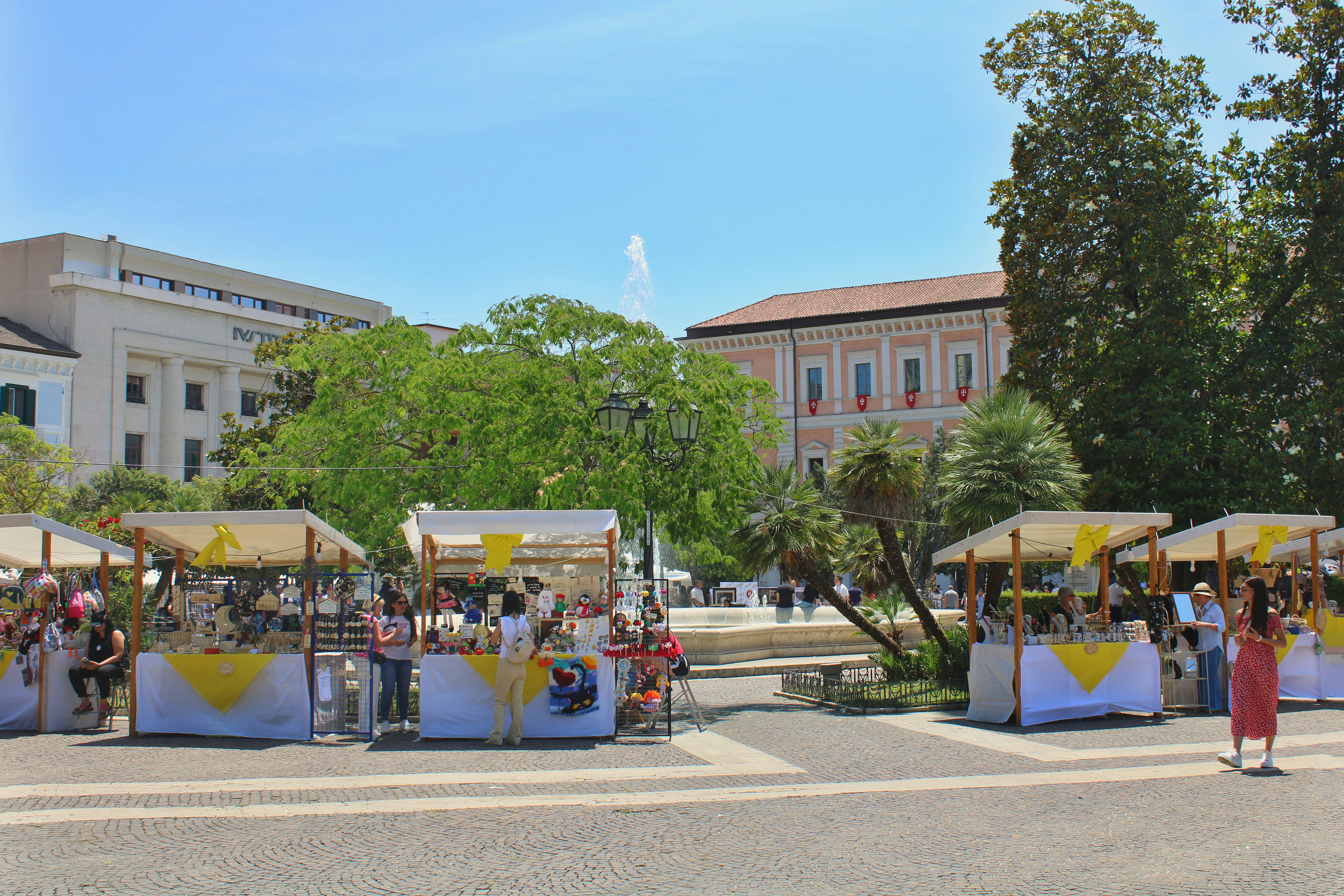 Outdoor market stalls with people browsing on a sunny day.