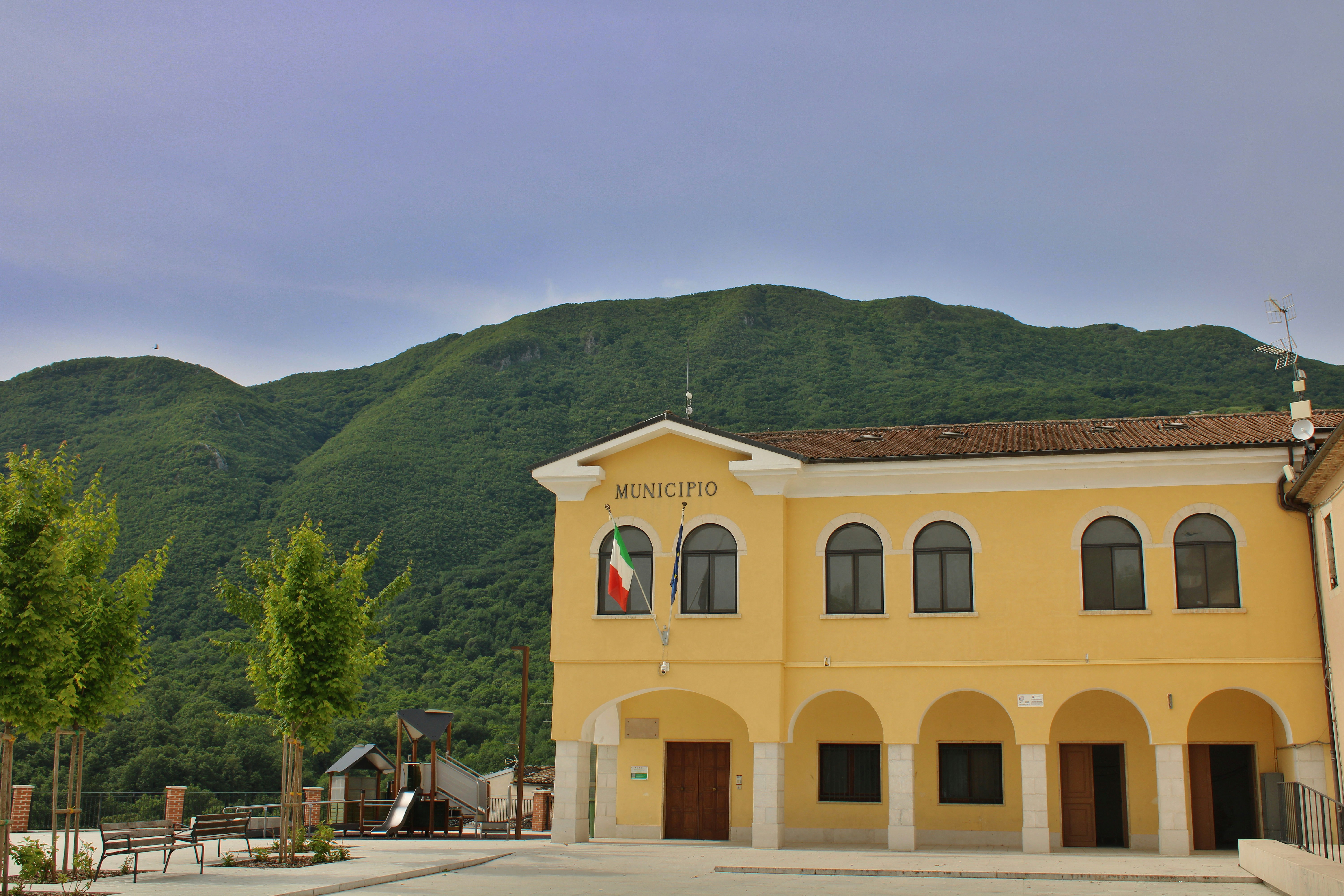 Yellow municipal building with italian flag and mountains.