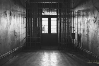 A dark, empty prison hallway with cell doors open.