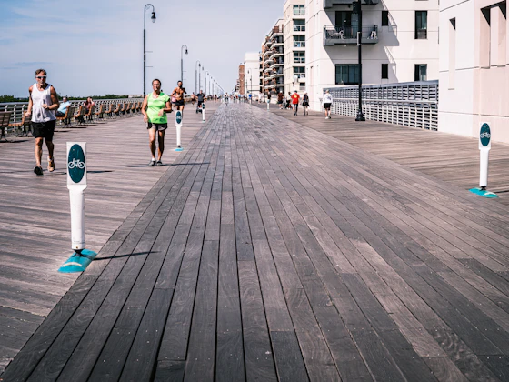 Grupo de corredores treinando em calçadão de madeira à beira do mar, com prédios residenciais ao fundo
