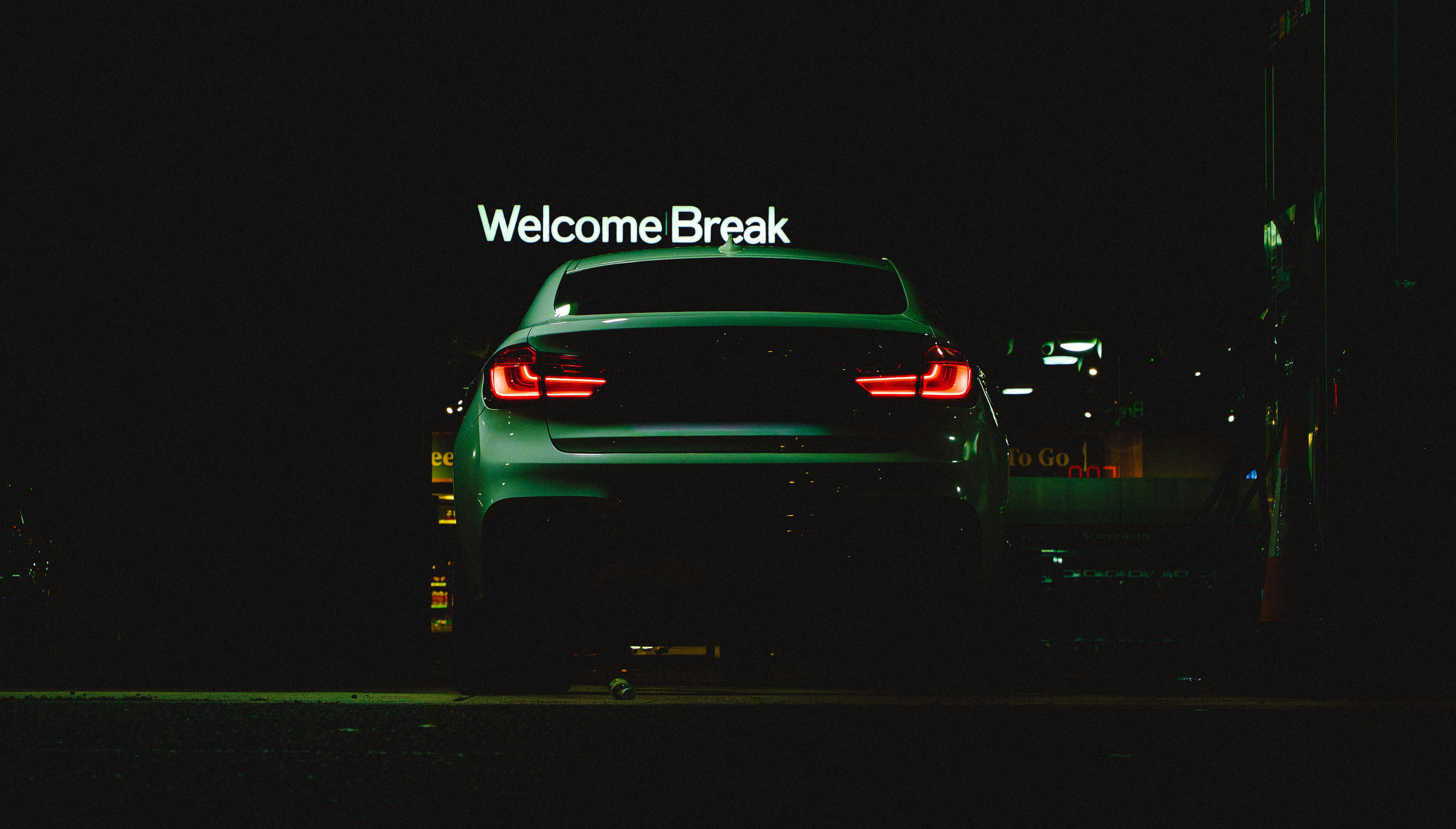 Car parked at night with "welcome break" sign.