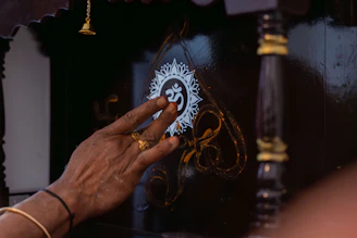 A hand touches an om symbol on a dark surface.