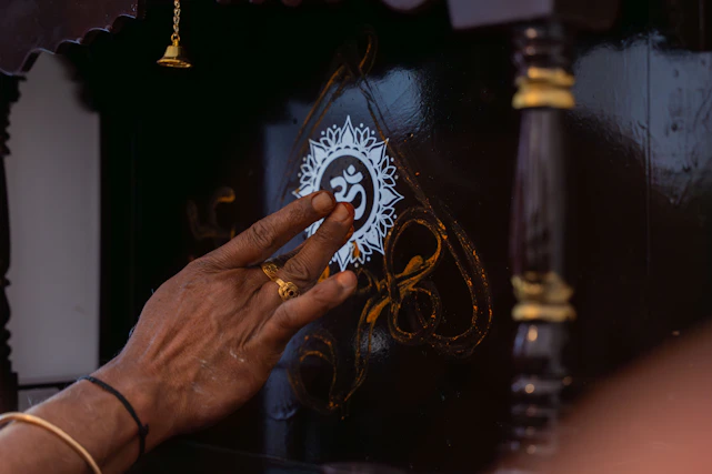 A hand touches an om symbol on a dark surface.