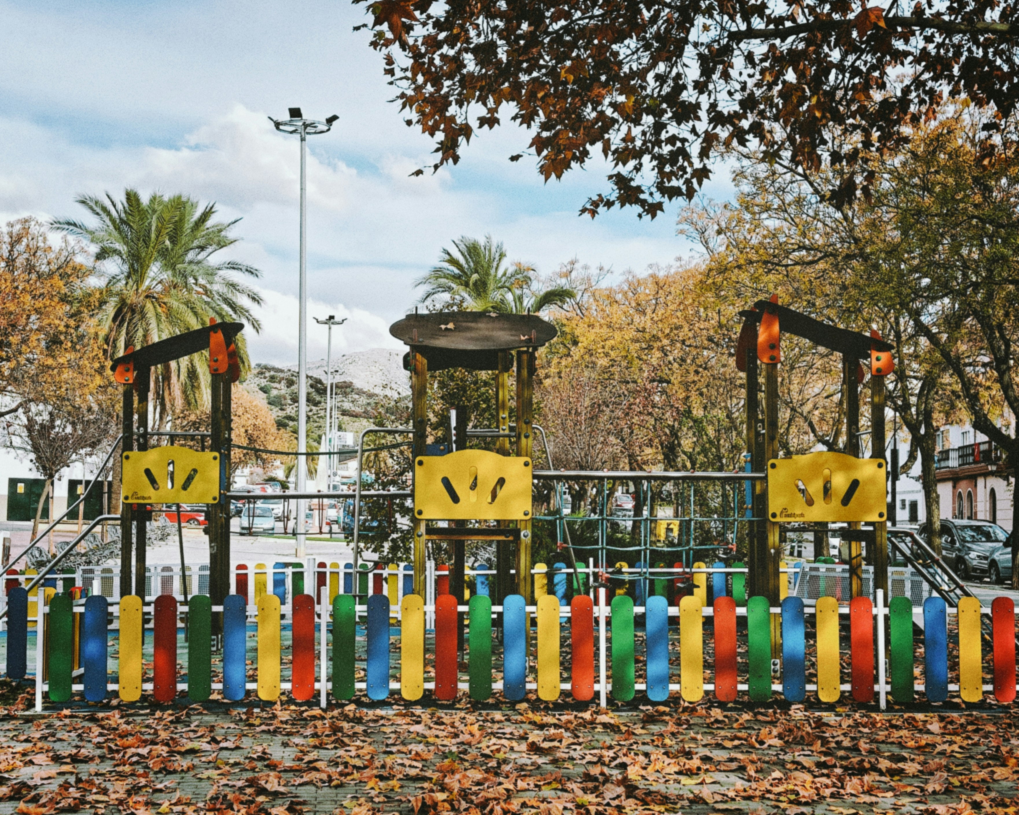 Colorful playground equipment behind a striped wooden fence.