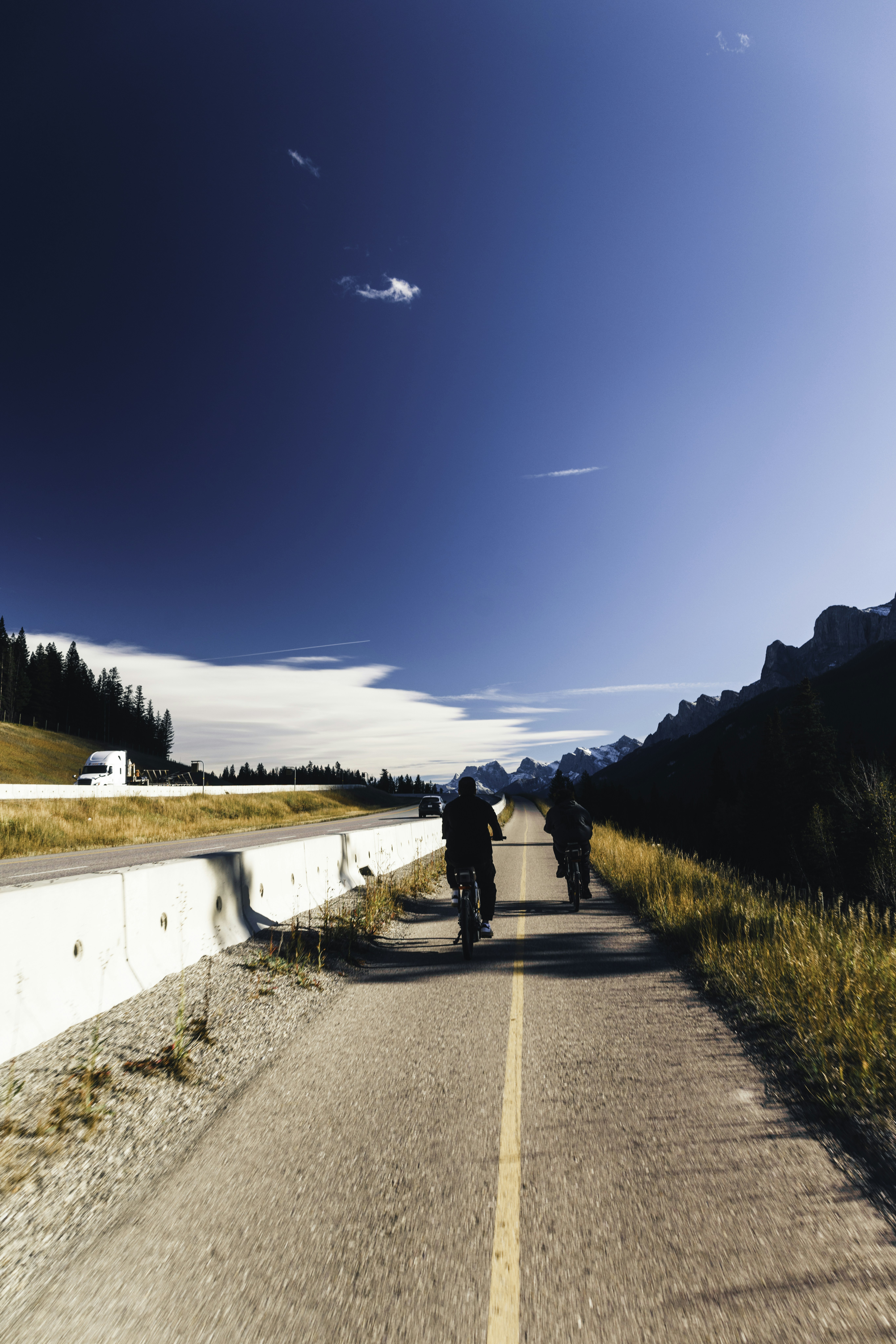 Two people cycle on a path beside a highway.