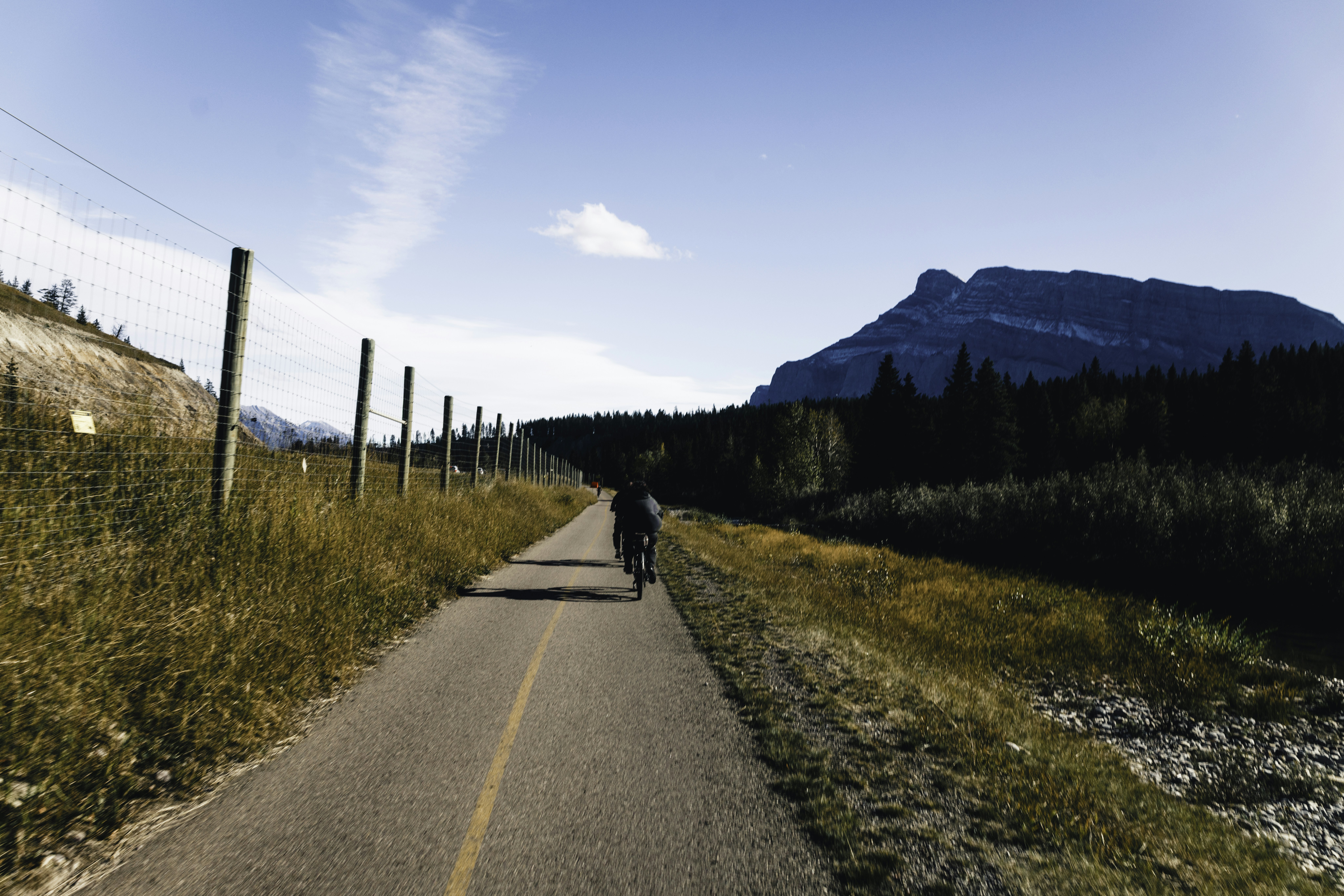 A person cycles down a paved path near mountains.