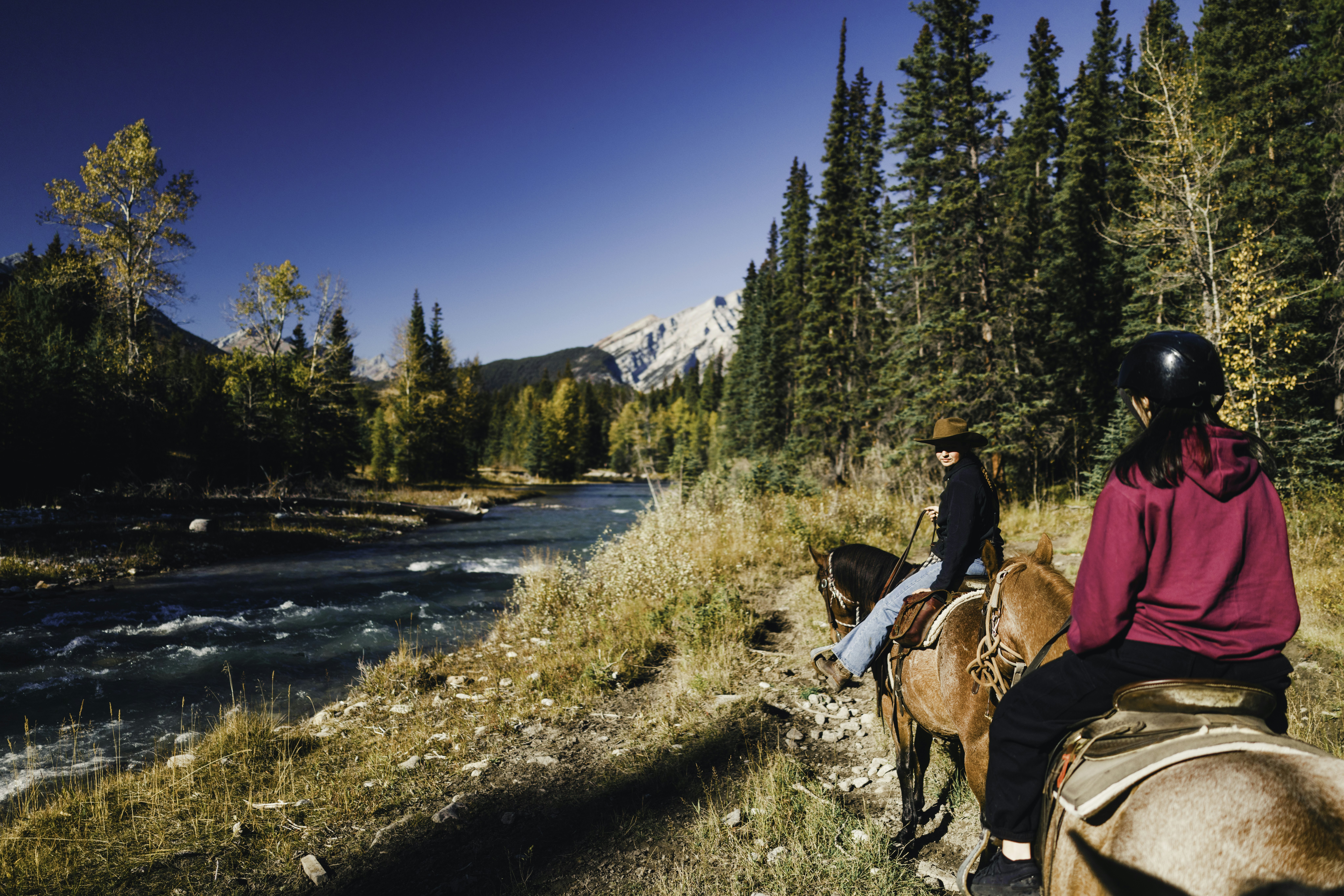Two people horseback riding along a river.
