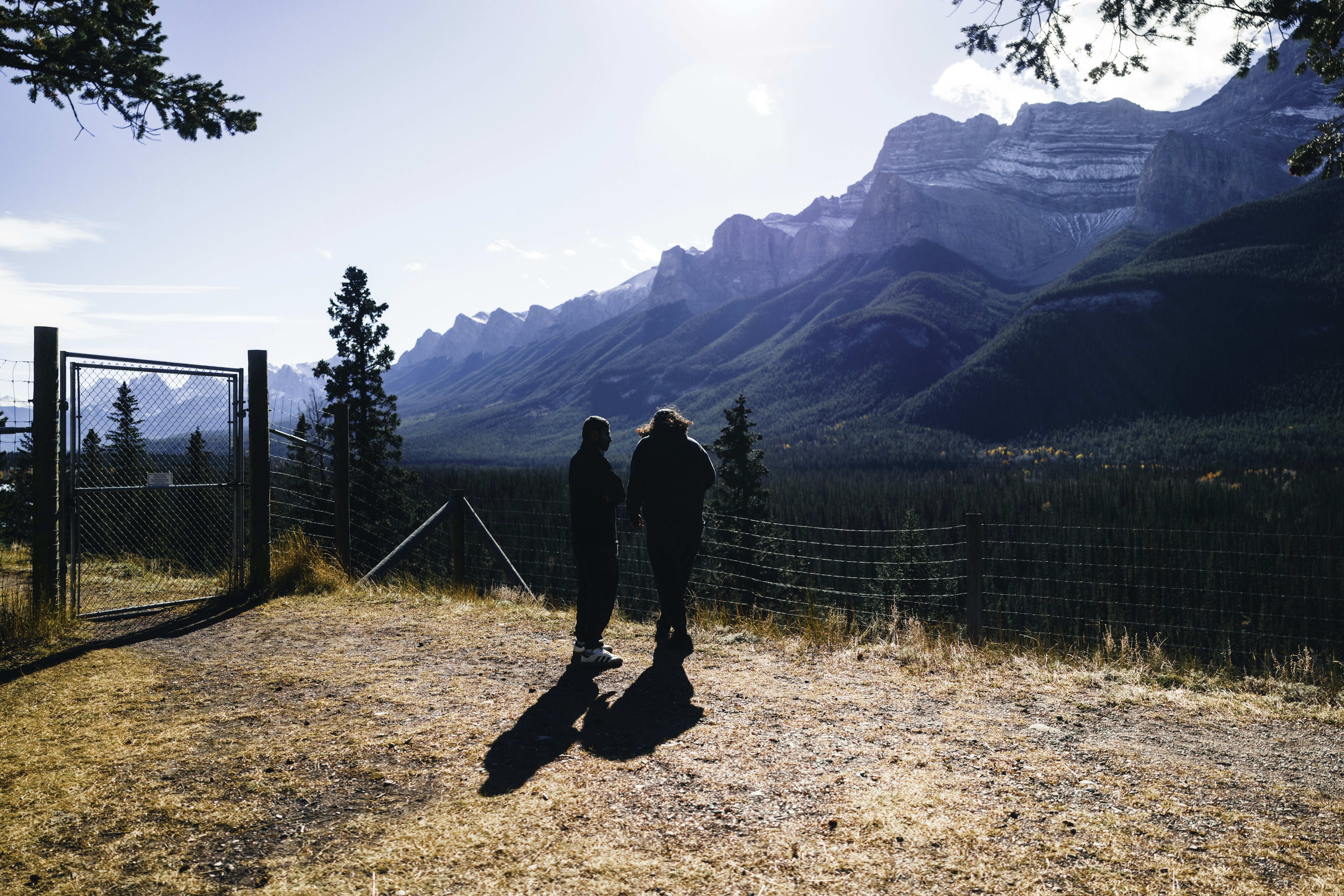 Two people stand on a hill overlooking mountains.