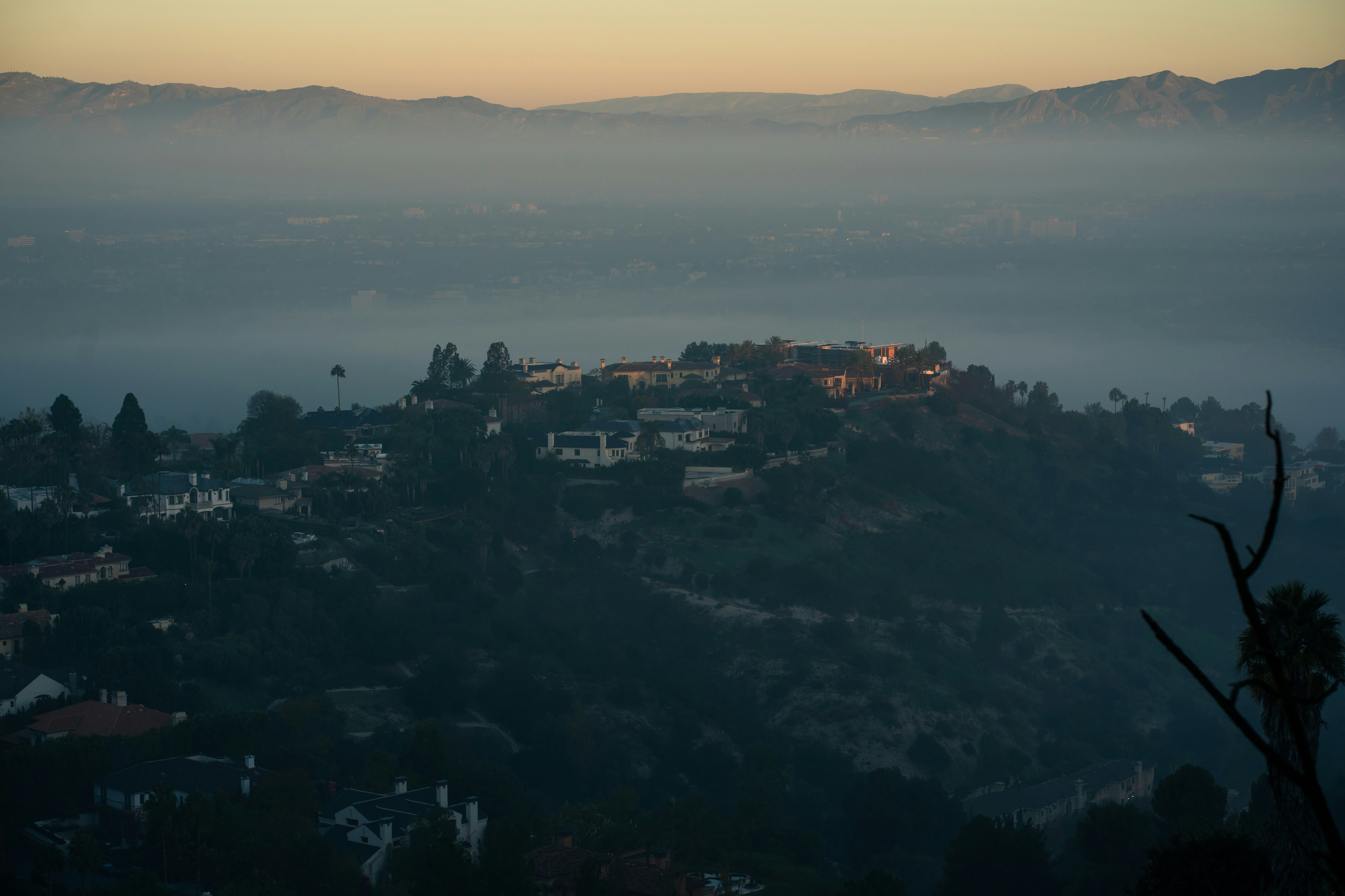 Hazy morning over a residential hilltop with distant mountains.