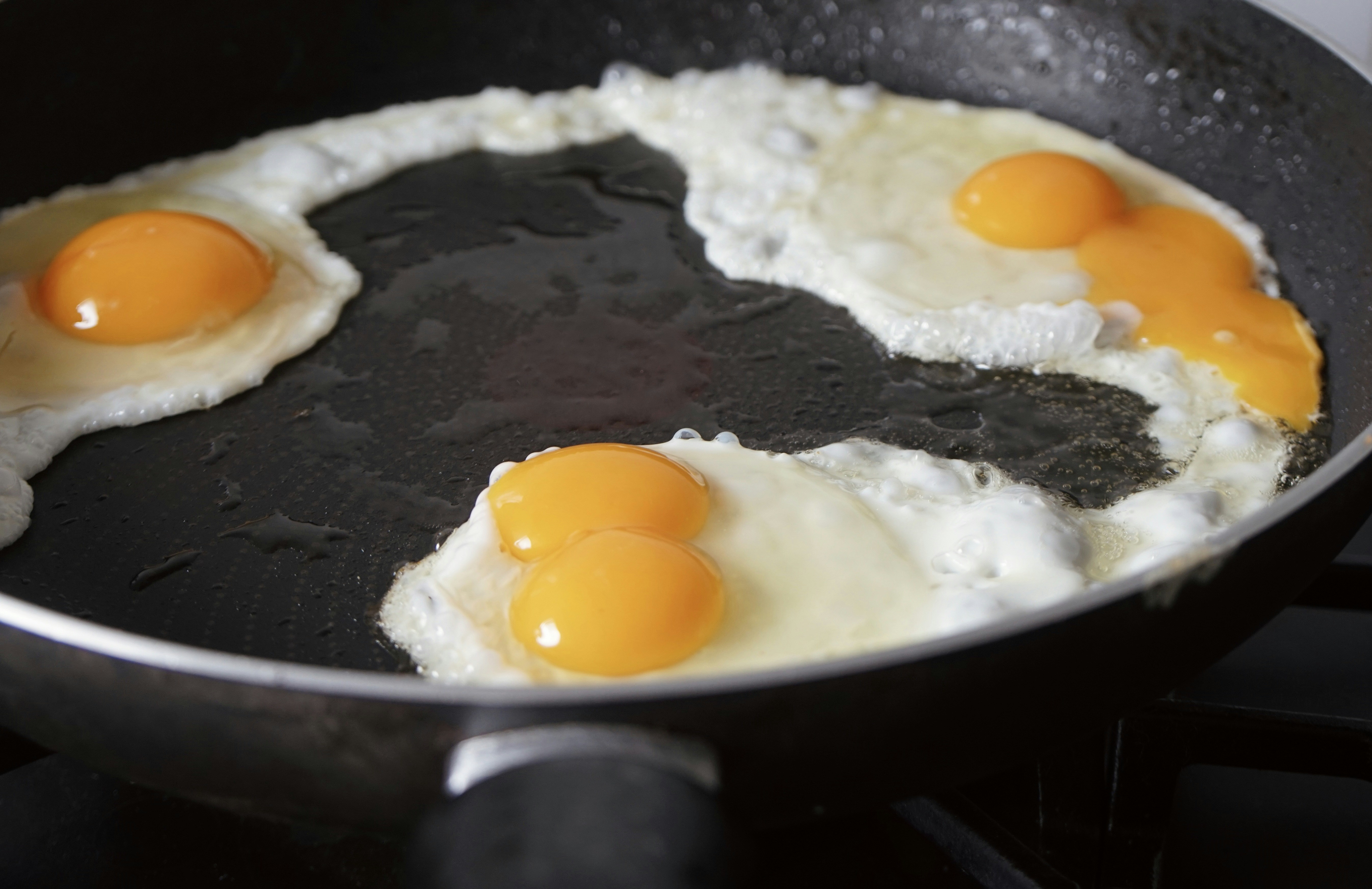 Three eggs frying in a black pan.