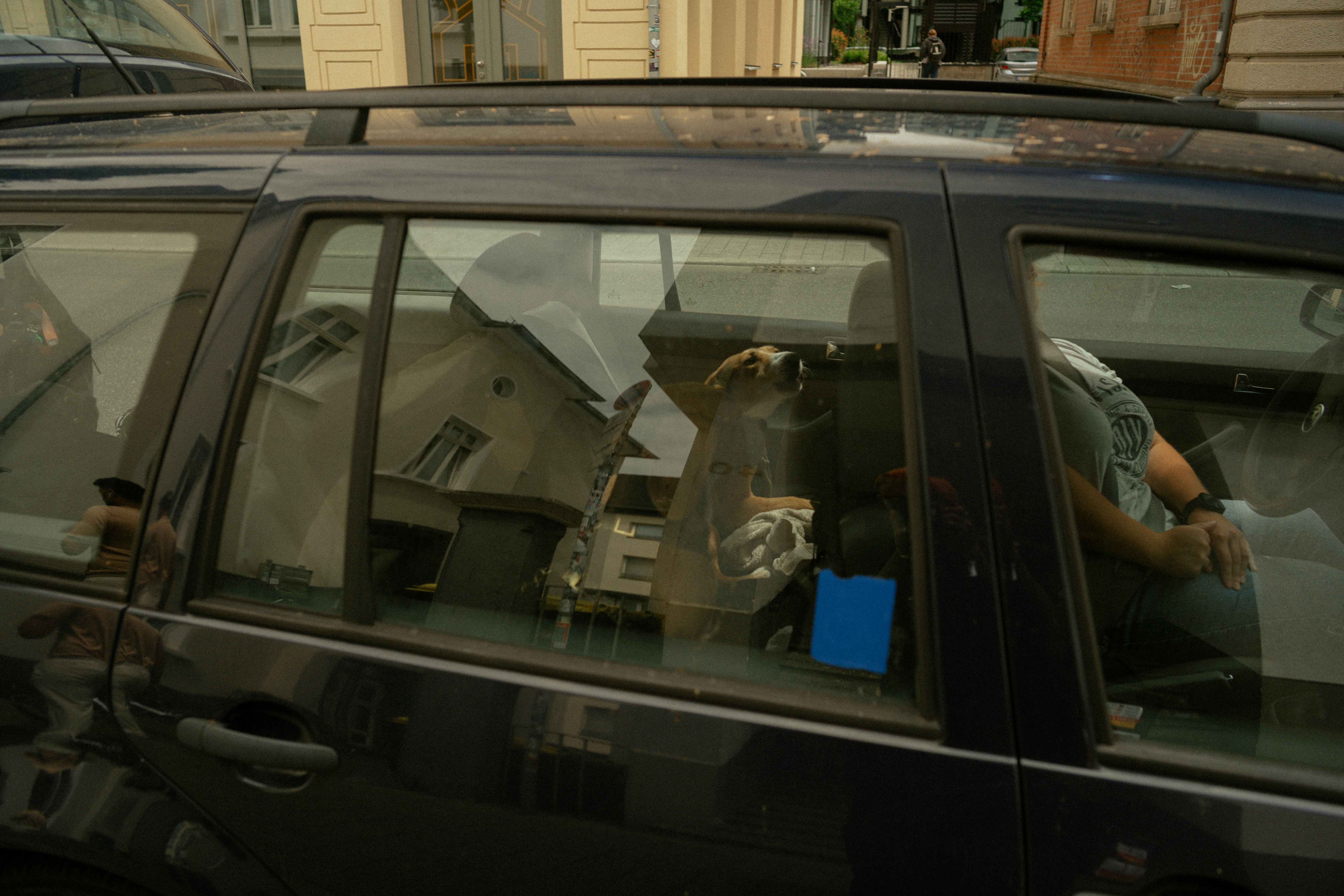 A car window reflects a person holding a camera.