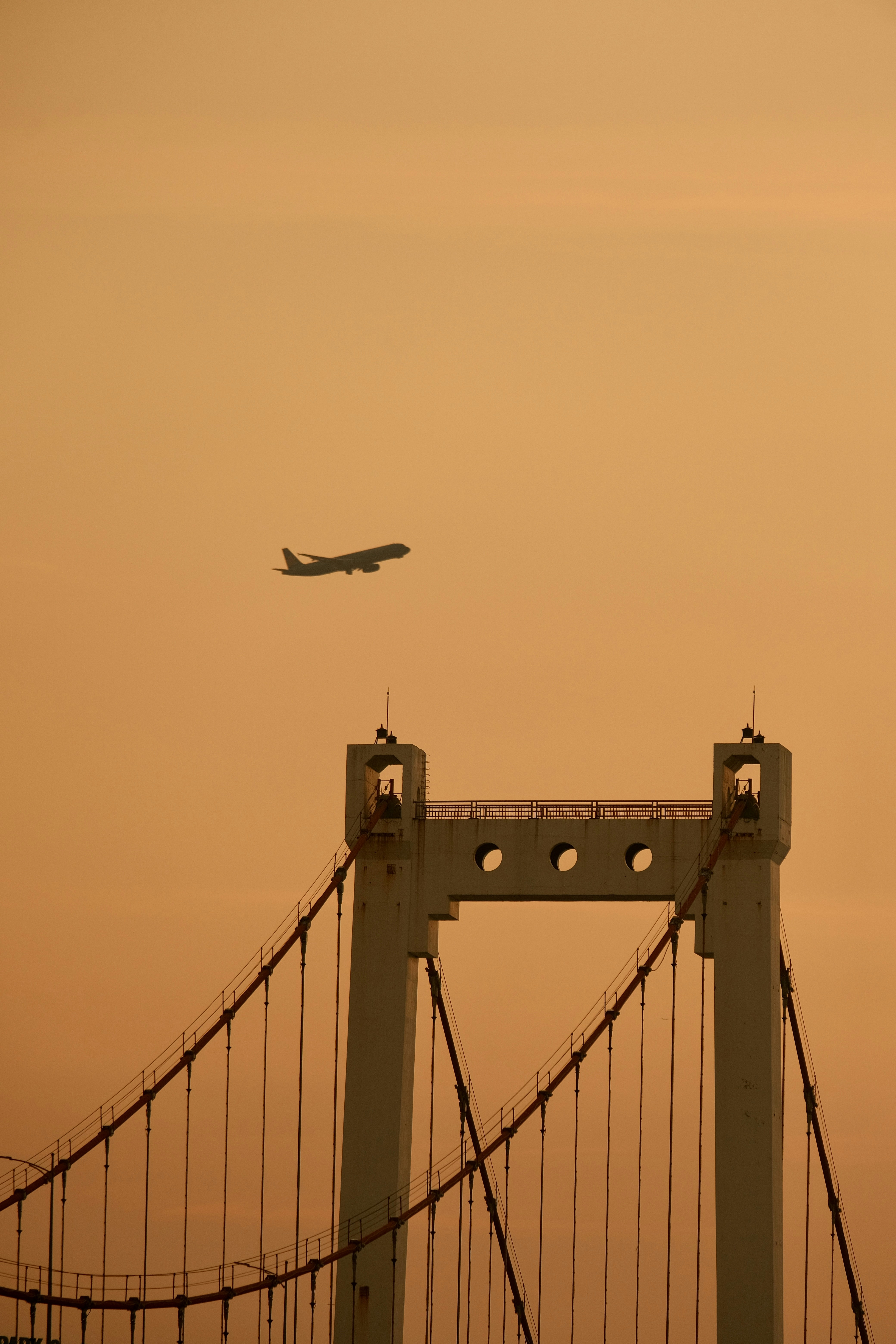 Airplane flying over suspension bridge at sunset