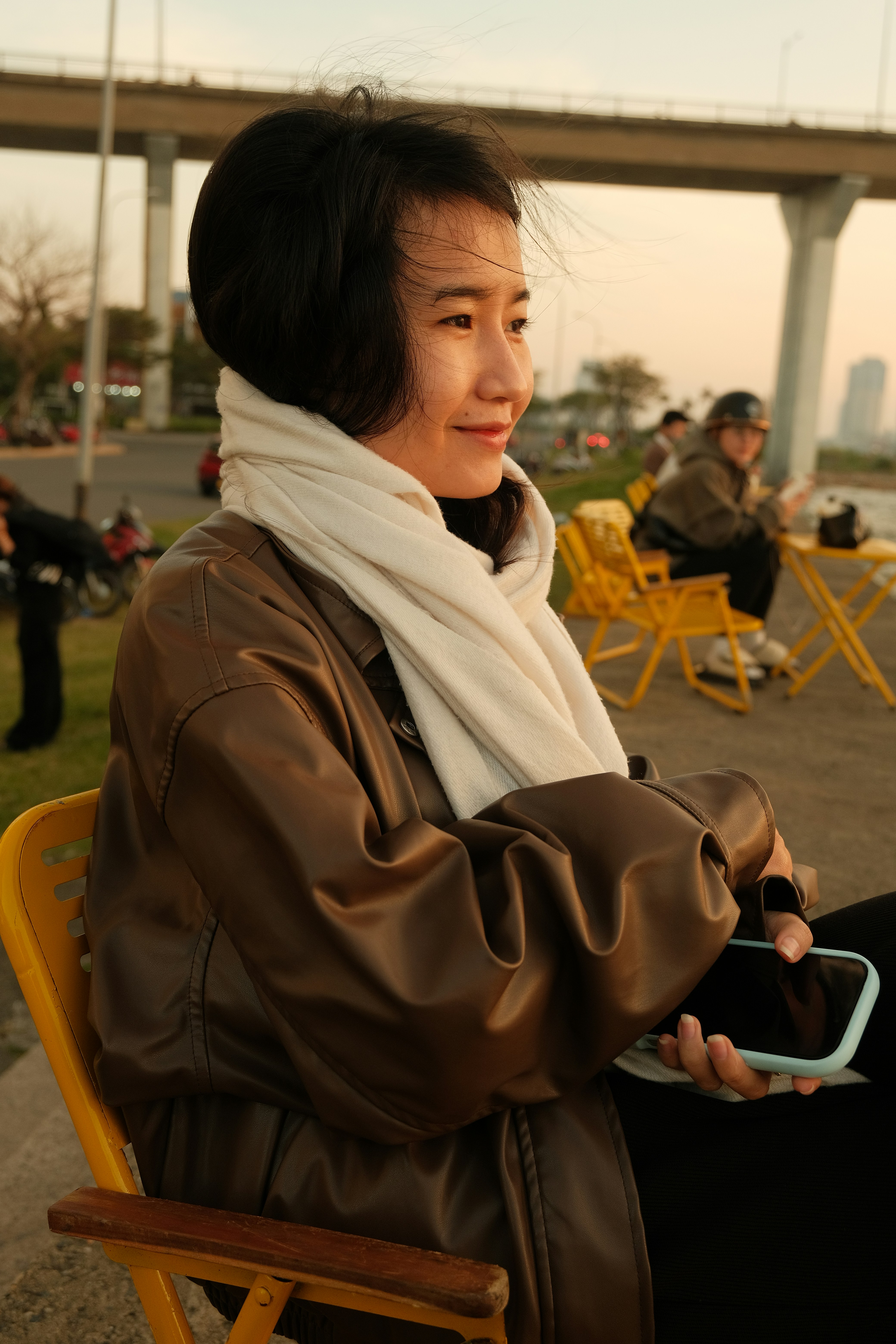 Young woman in a brown jacket and white scarf outdoors.