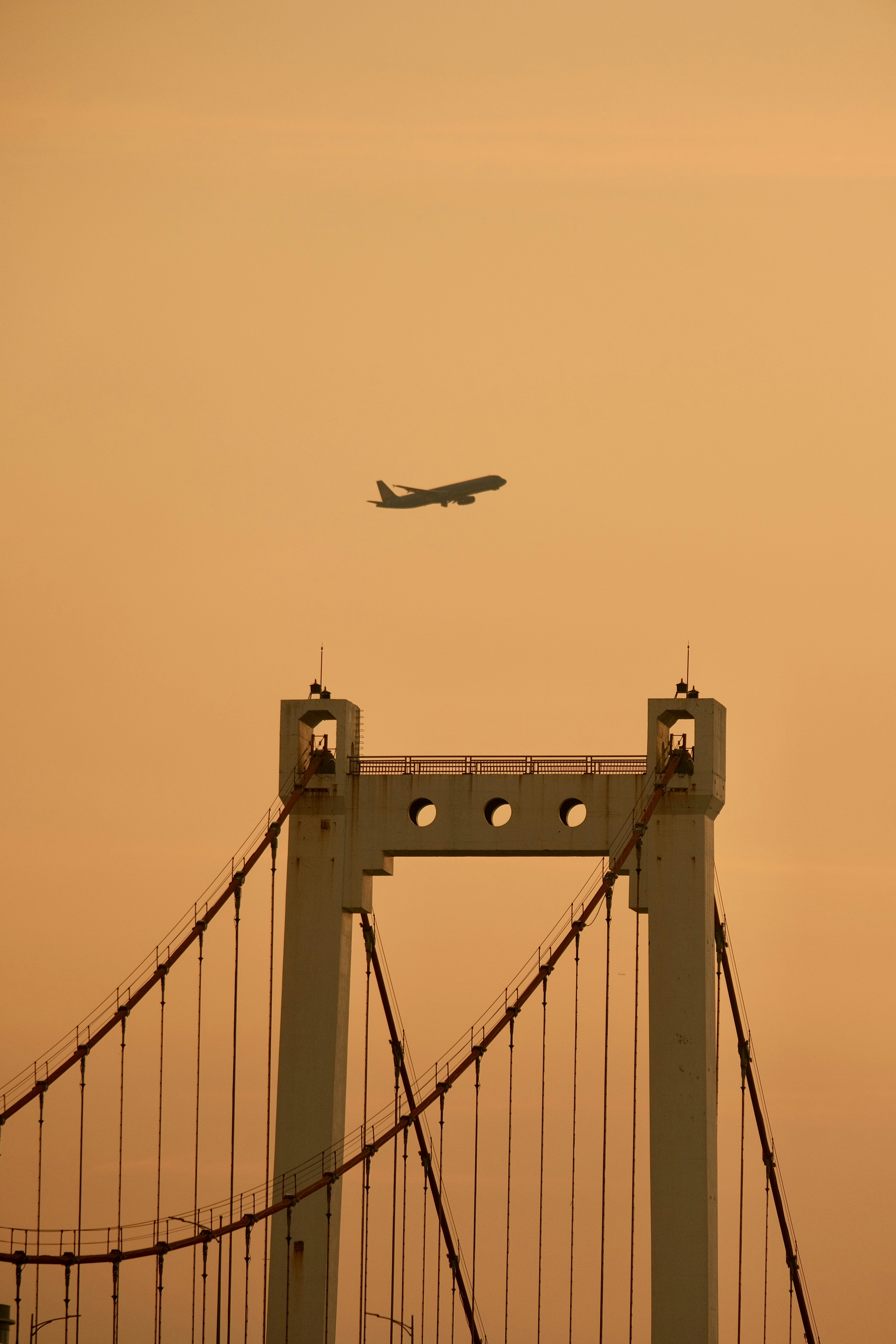 Airplane flying over a suspension bridge at sunset