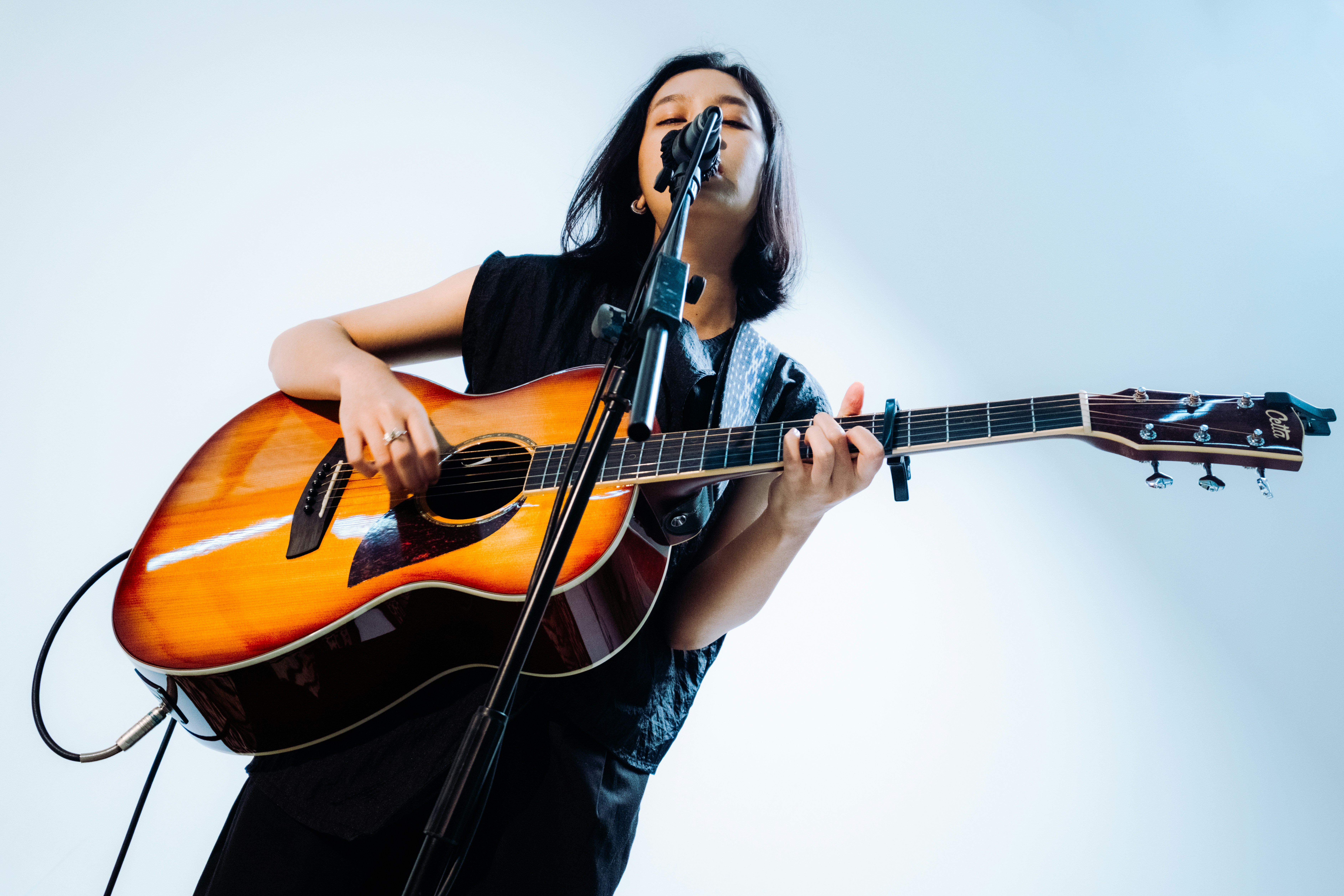A woman singing while playing an acoustic guitar.