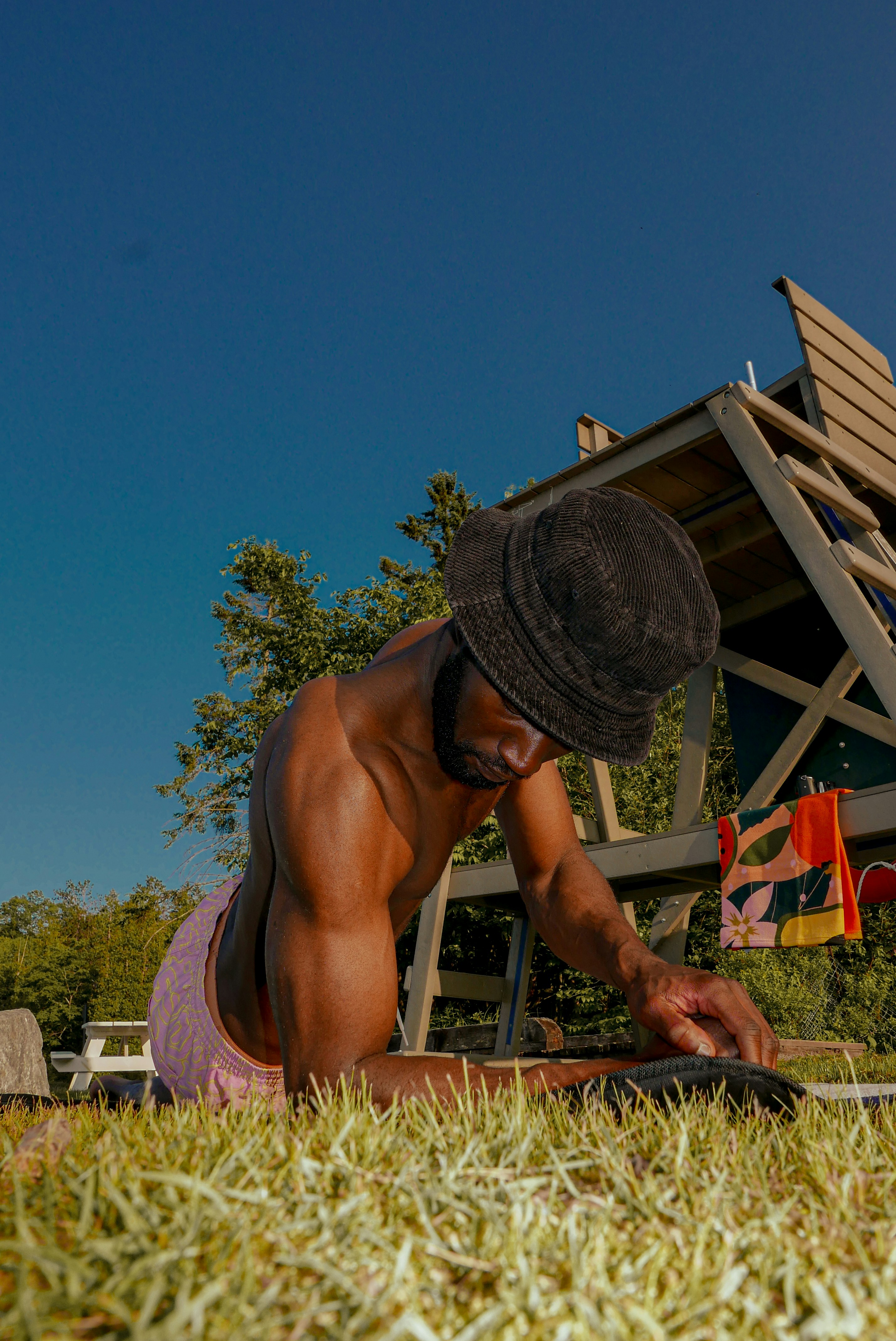 Man in bucket hat lying on grass by playground
