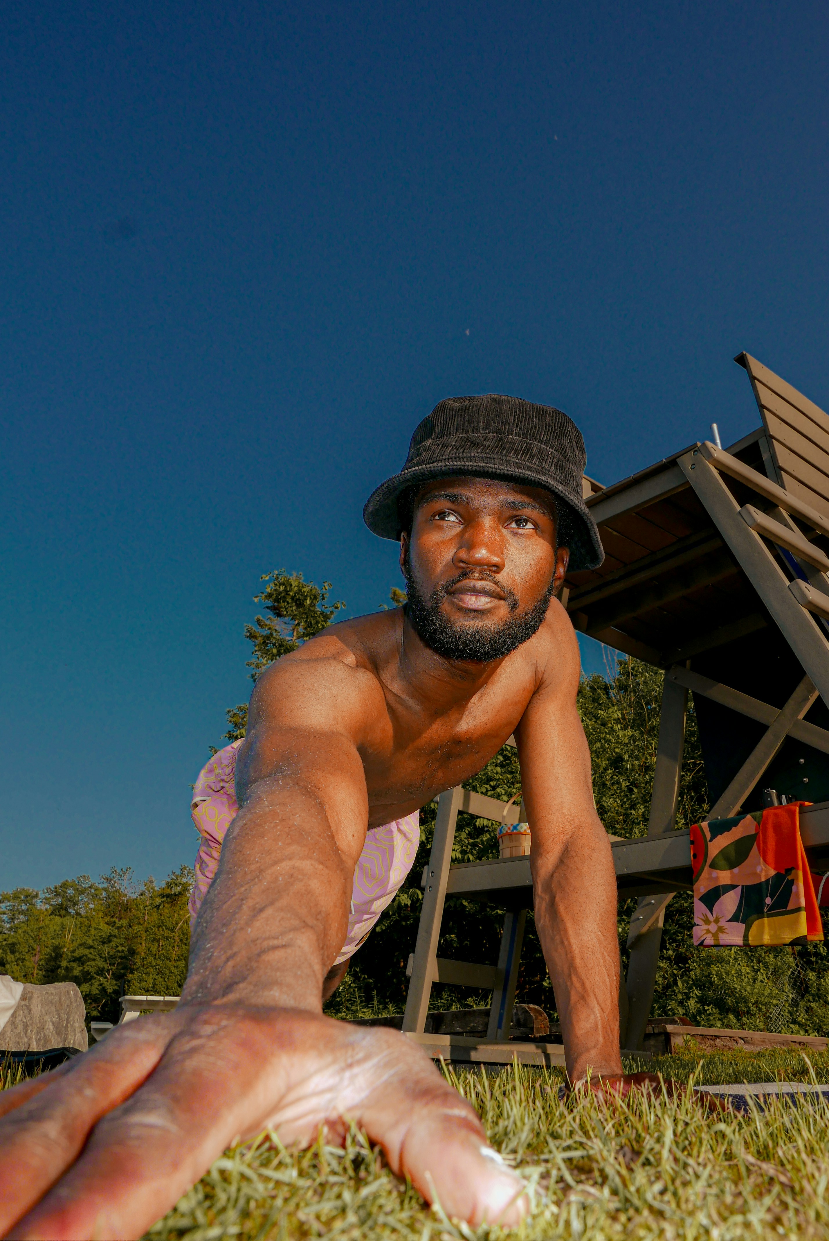 Man in bucket hat crawling on grass with wooden structure
