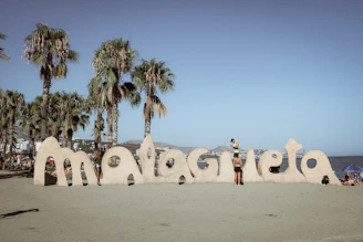 Large letters spell out malaga on a sandy beach.