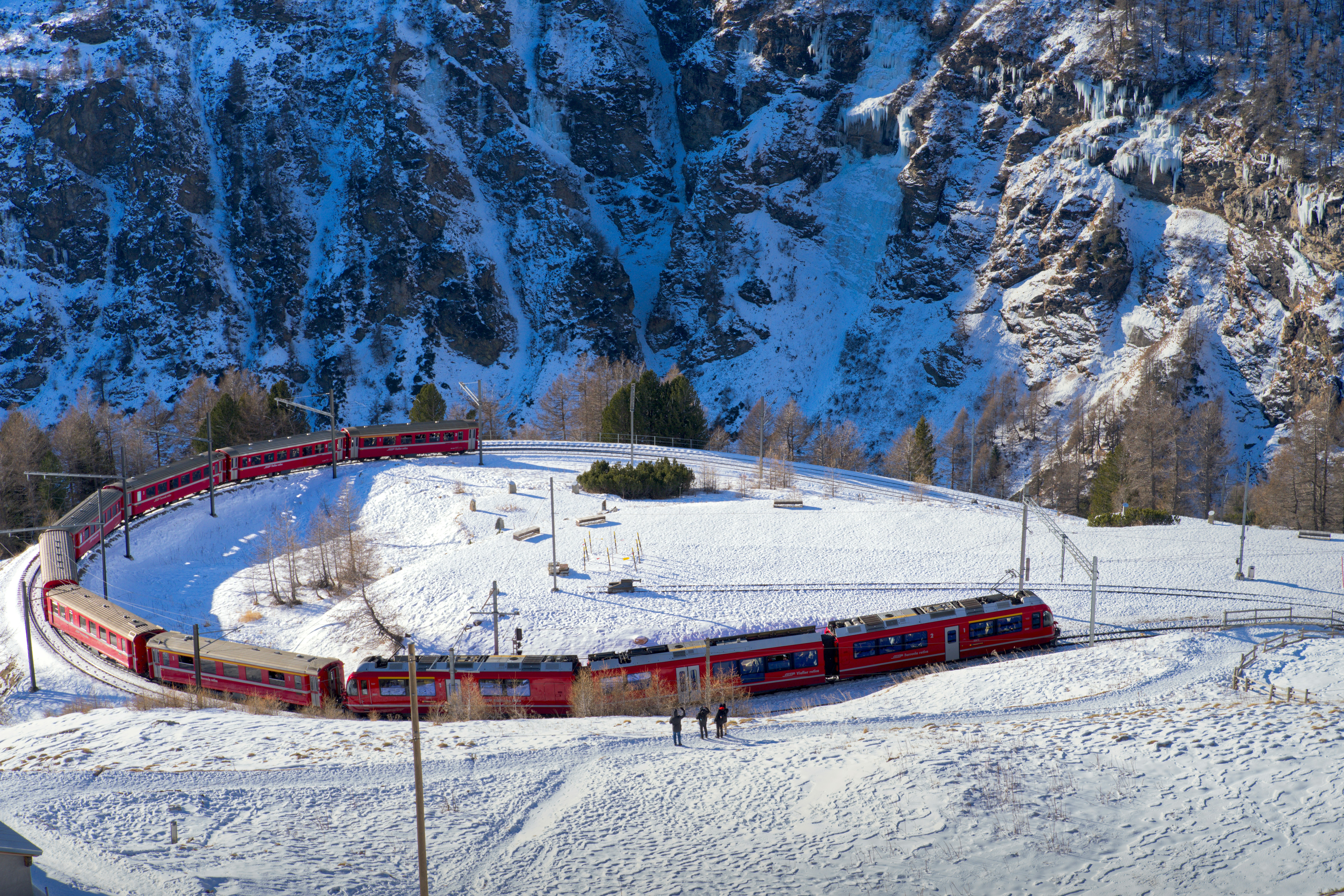 Red train on a snowy spiral track in mountains.