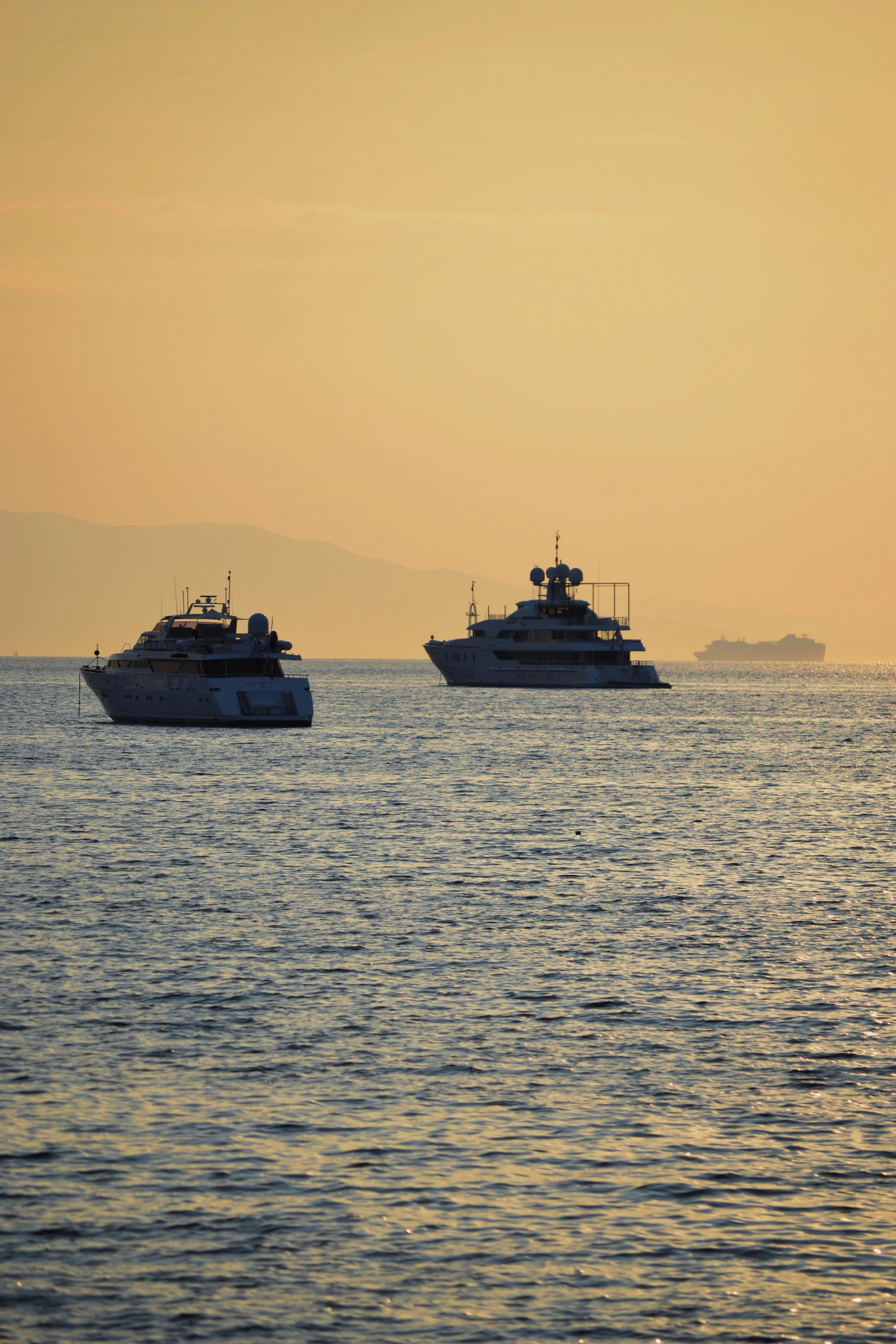 Two superyachts lying at anchor in calm water at sunset off the French Riviera