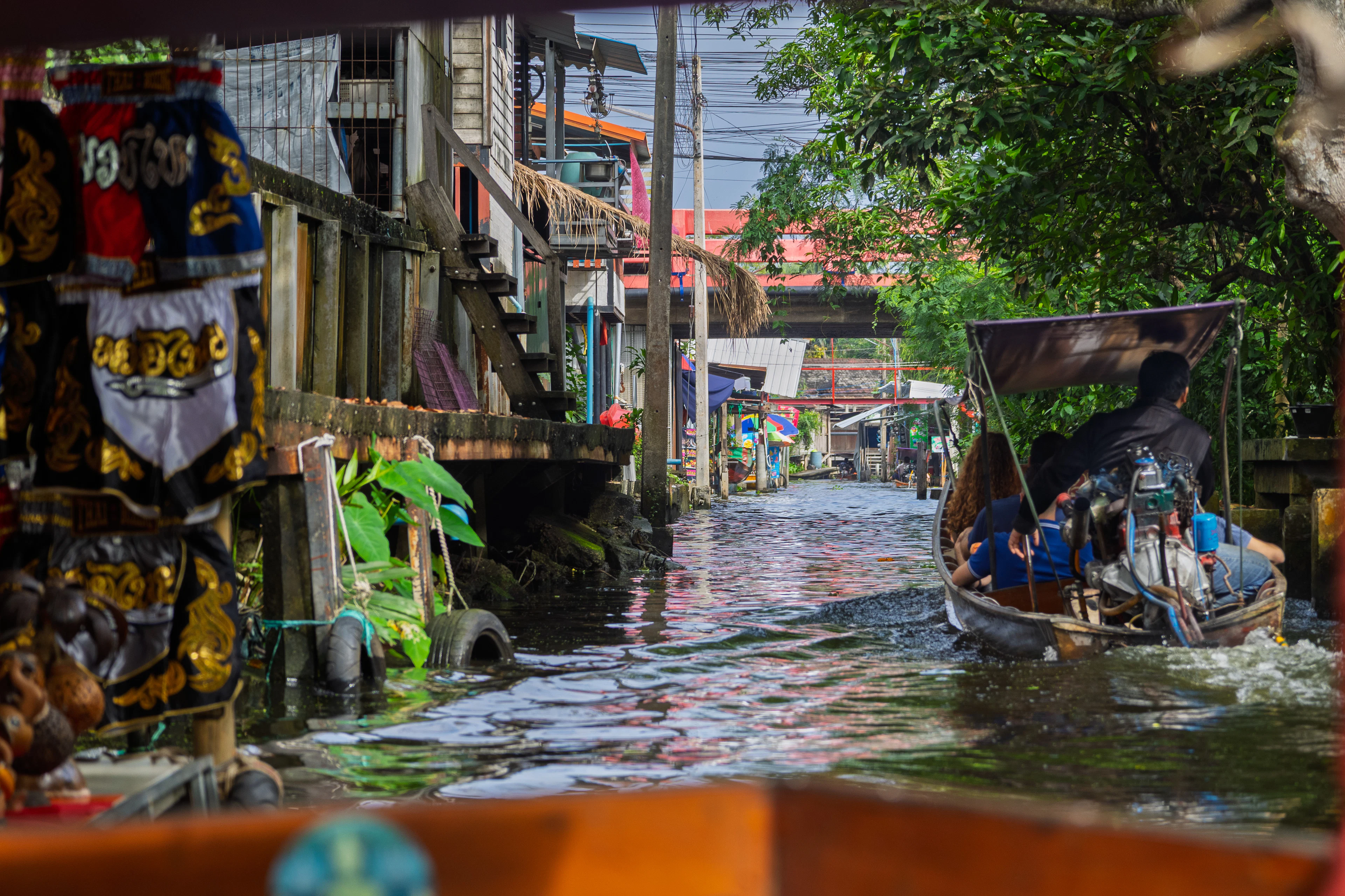A longtail boat in a narrow canal between wooden stilt houses in Bangkok