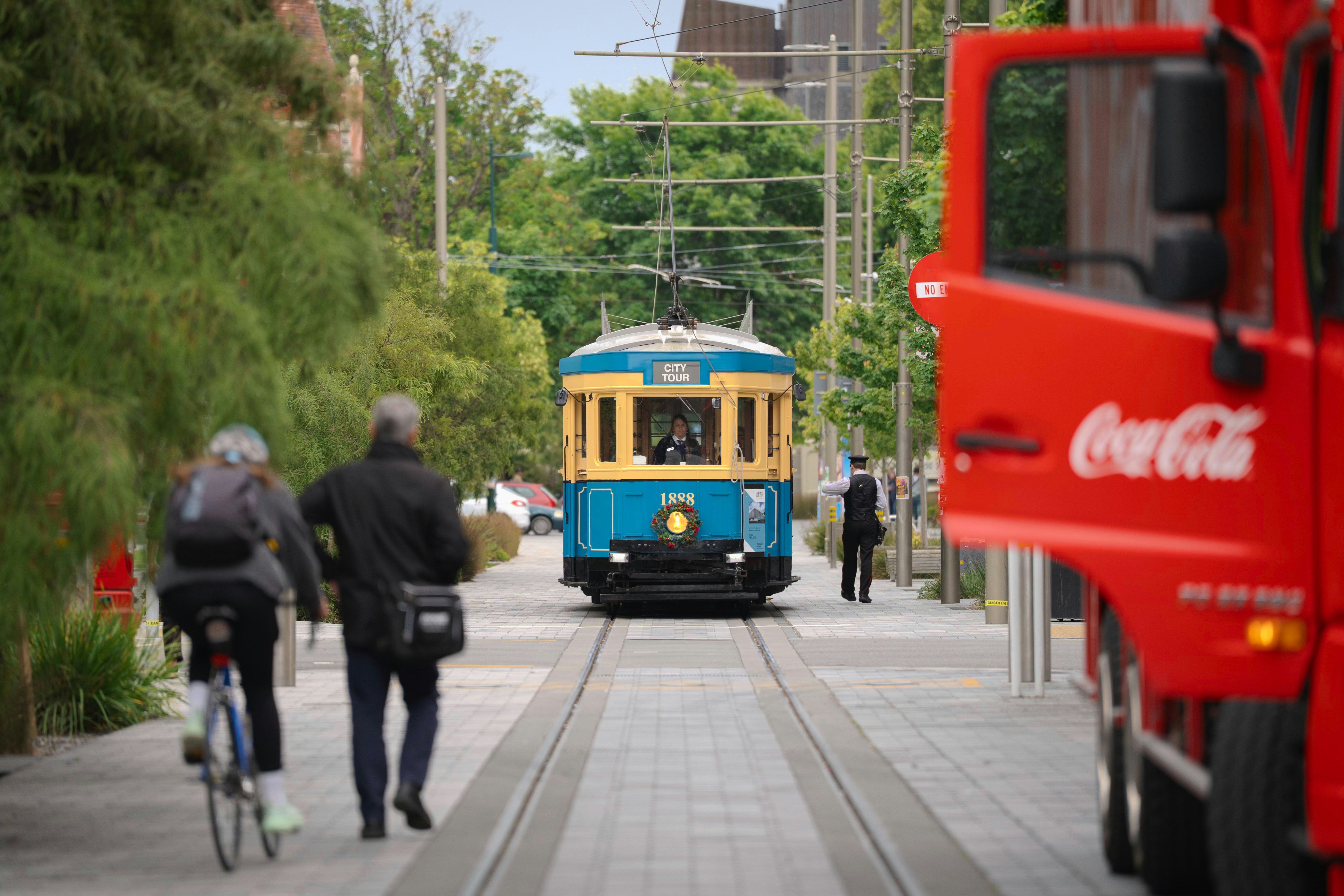 A blue tram approaches people on a street.