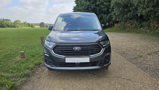 Dark grey van parked on gravel path outdoors.