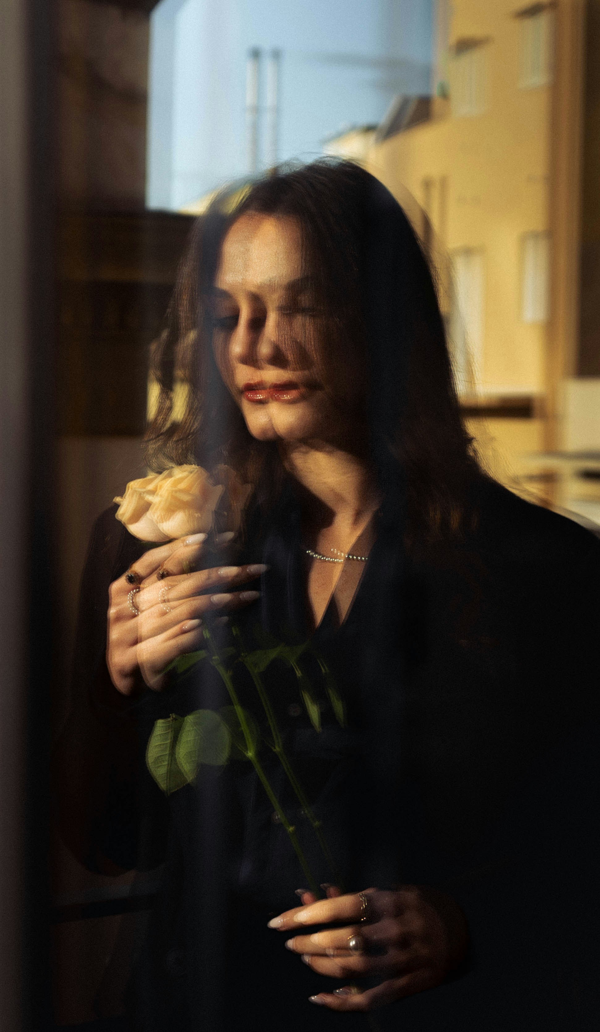 Frau, die eine einzelne blasse Rose mit geschlossenen Augen hält.