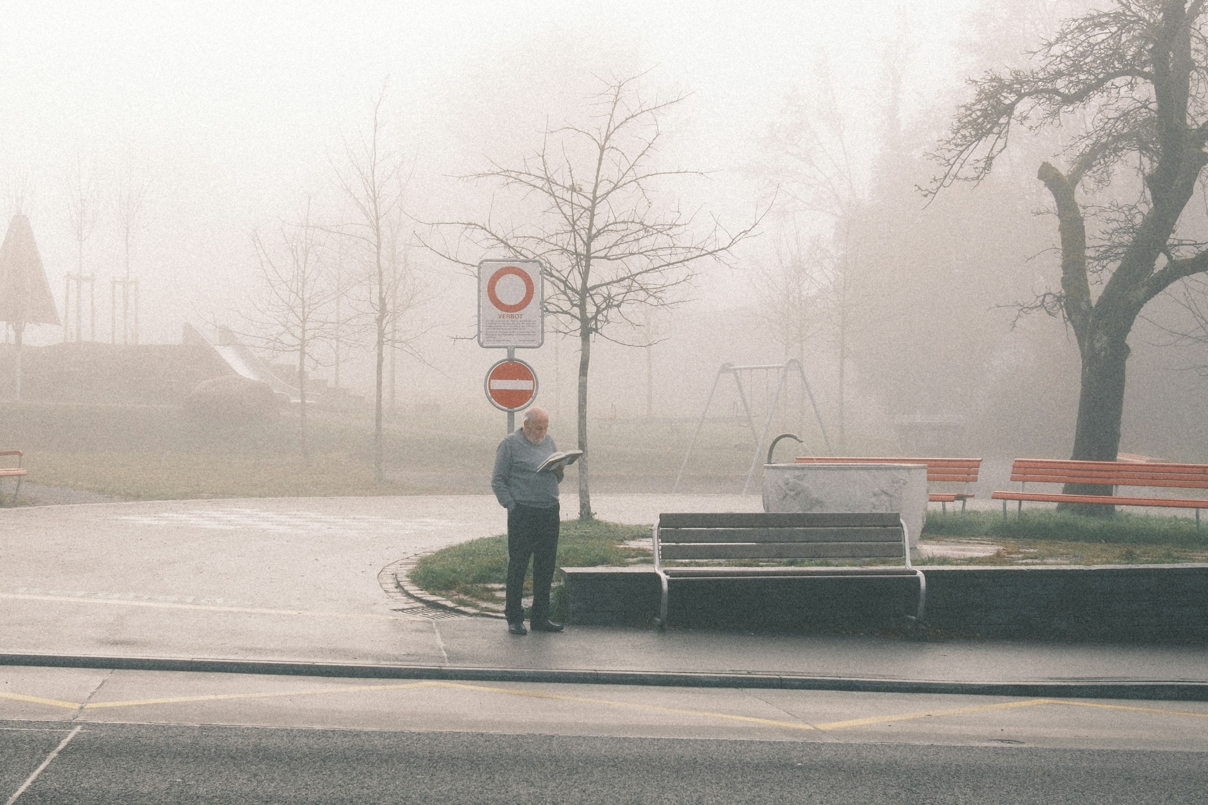 Un homme lisant un journal dans un parc brumeux.
