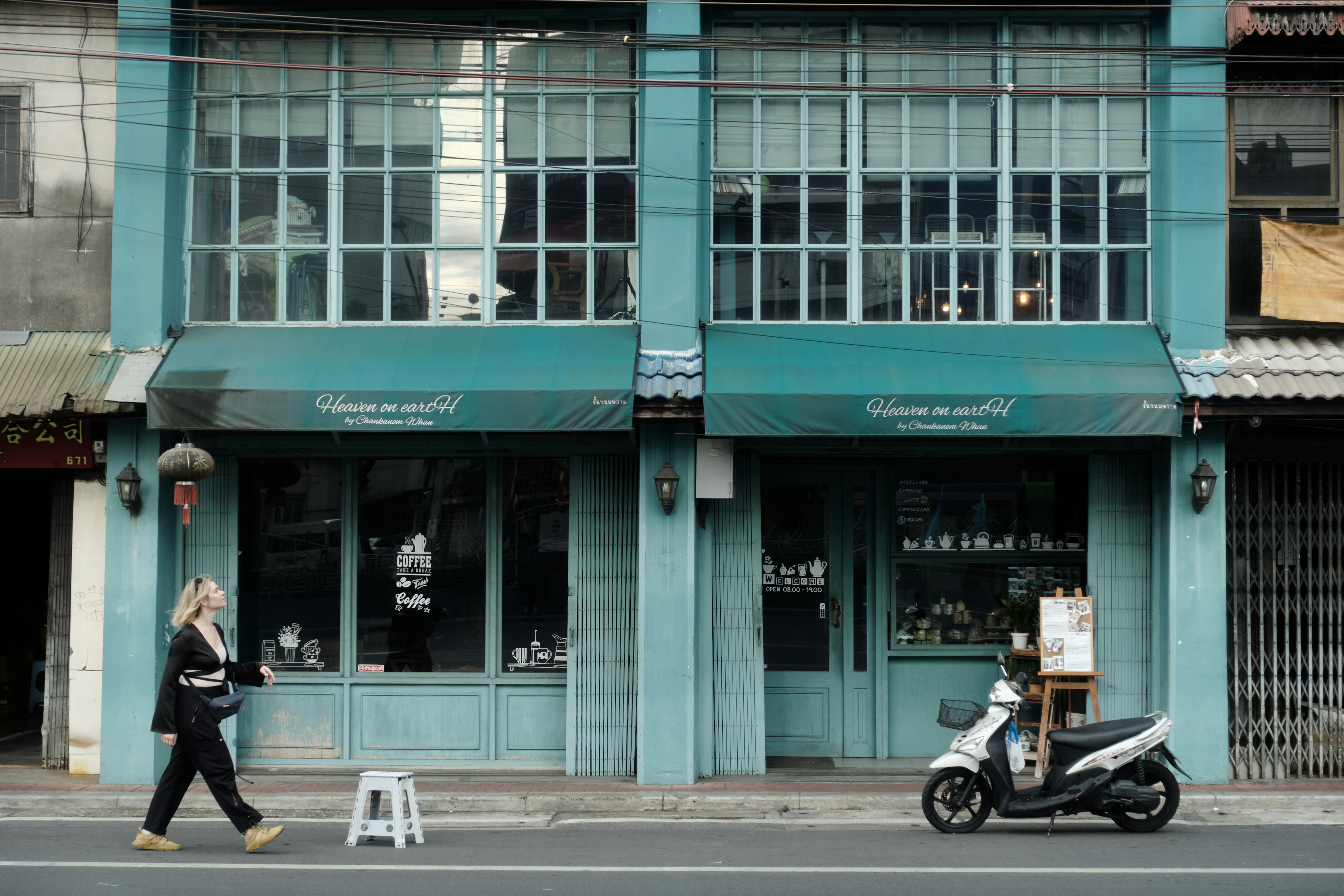 Une femme passe devant un immeuble turcelle avec un scooter.