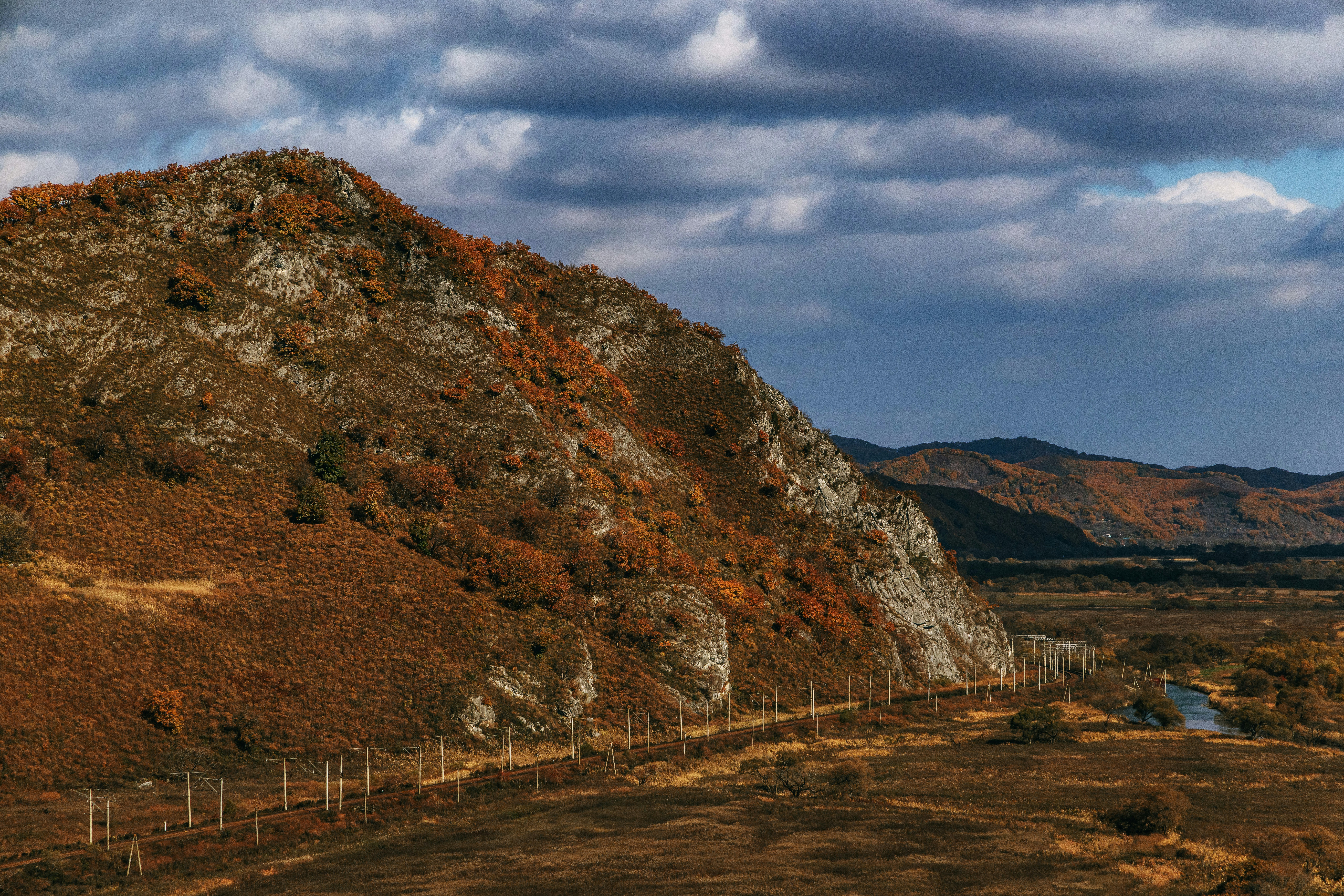 曇り空の下、秋の紅葉が広がる岩だらけの丘陵