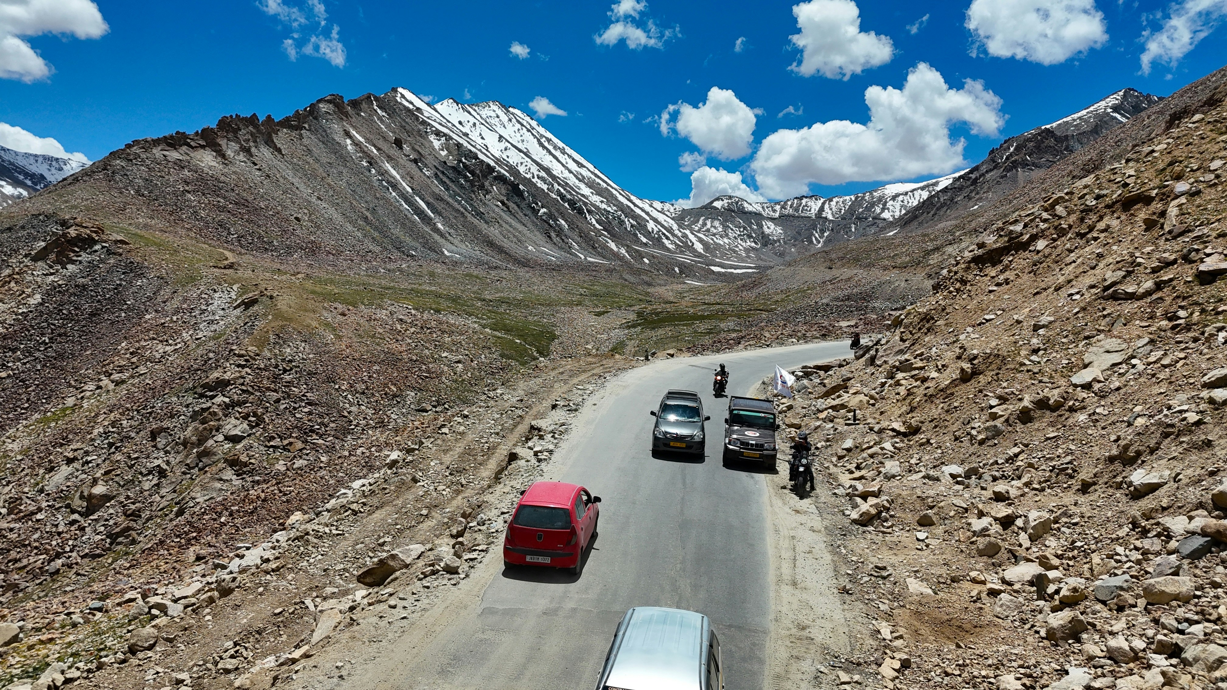 Cars driving on a winding mountain road under blue sky.