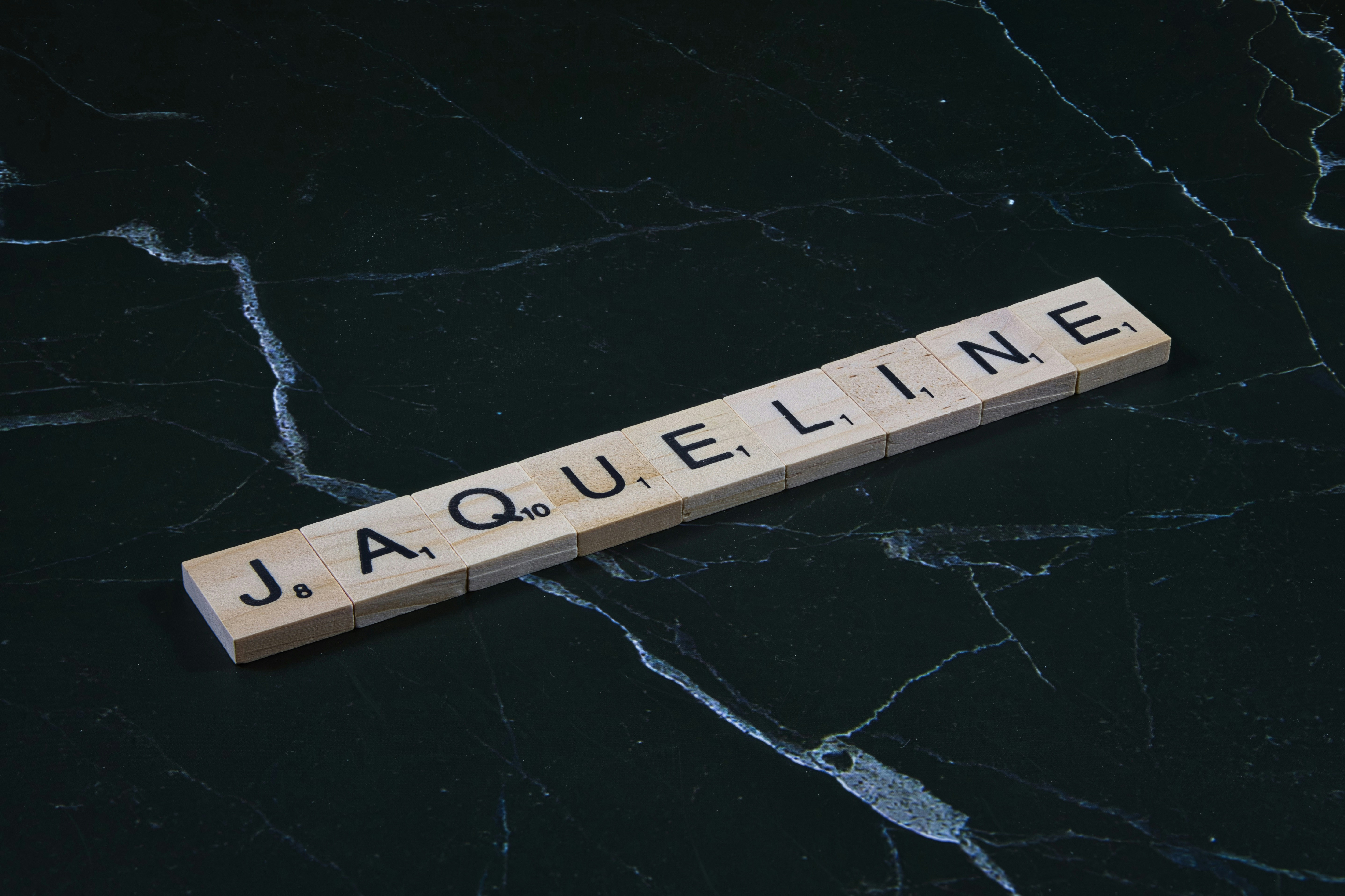 Wooden tiles spell out the name jacqueline on marble.
