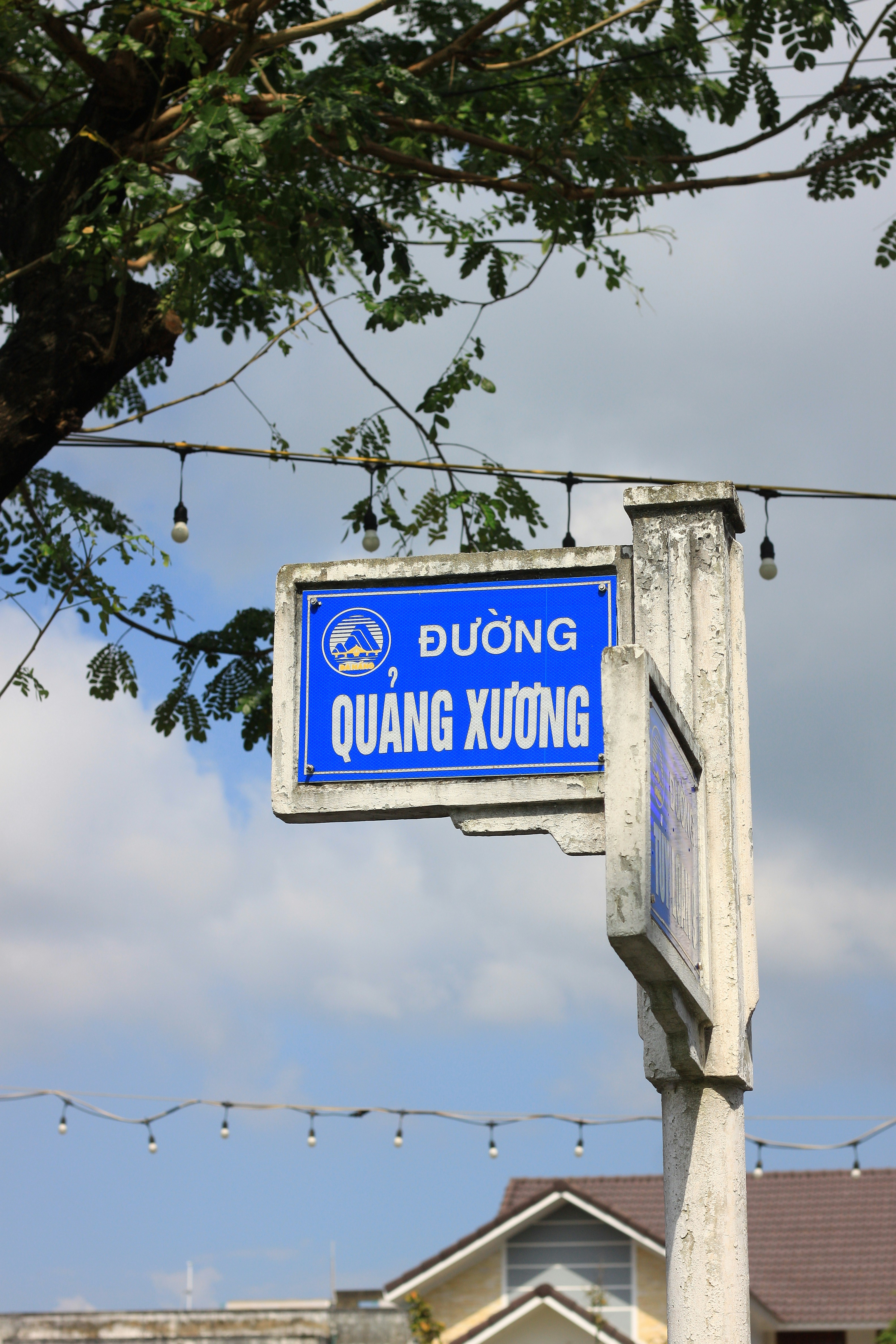 Blue street sign with vietnamese text against sky.