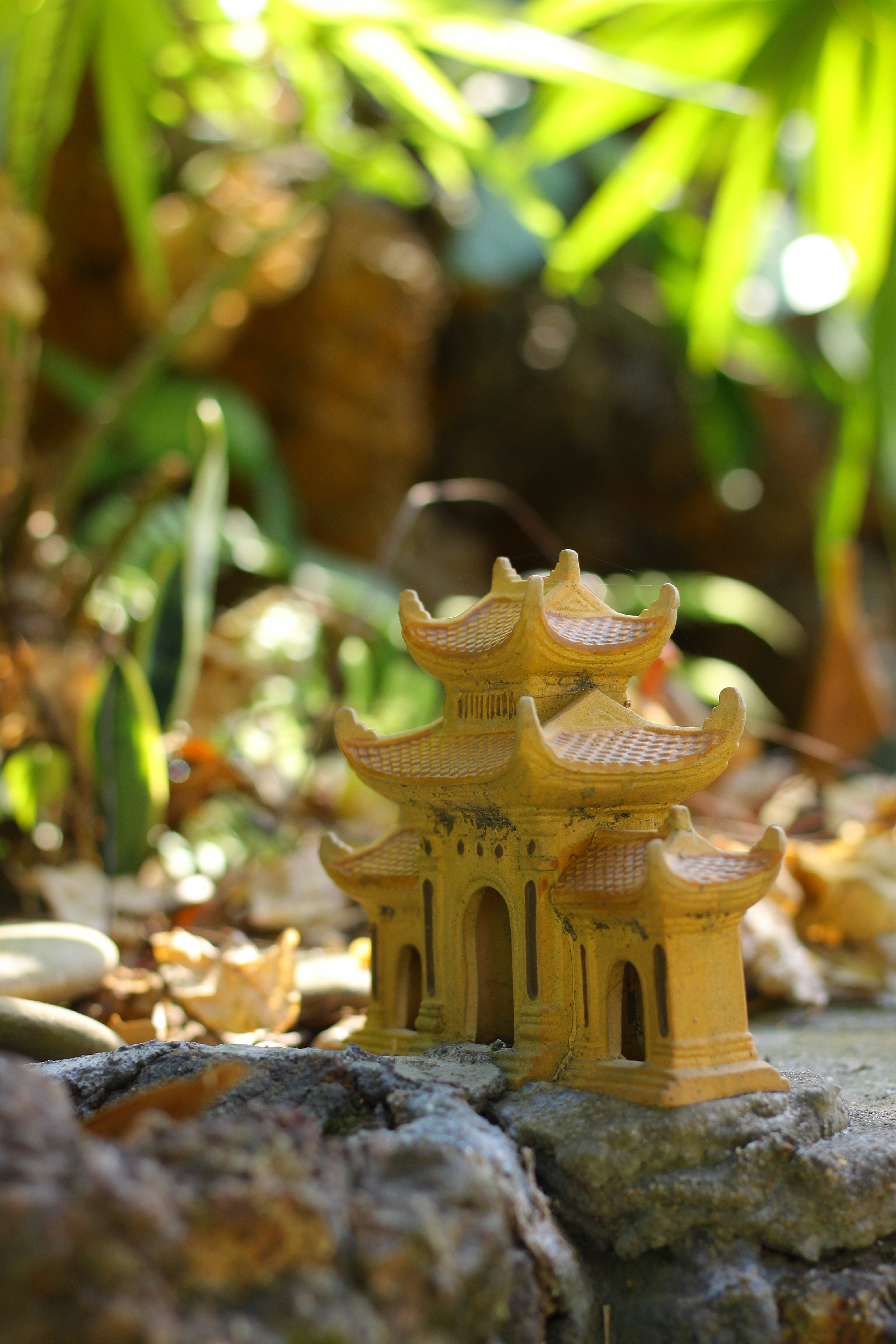 Miniature yellow pagoda structure in a garden setting.