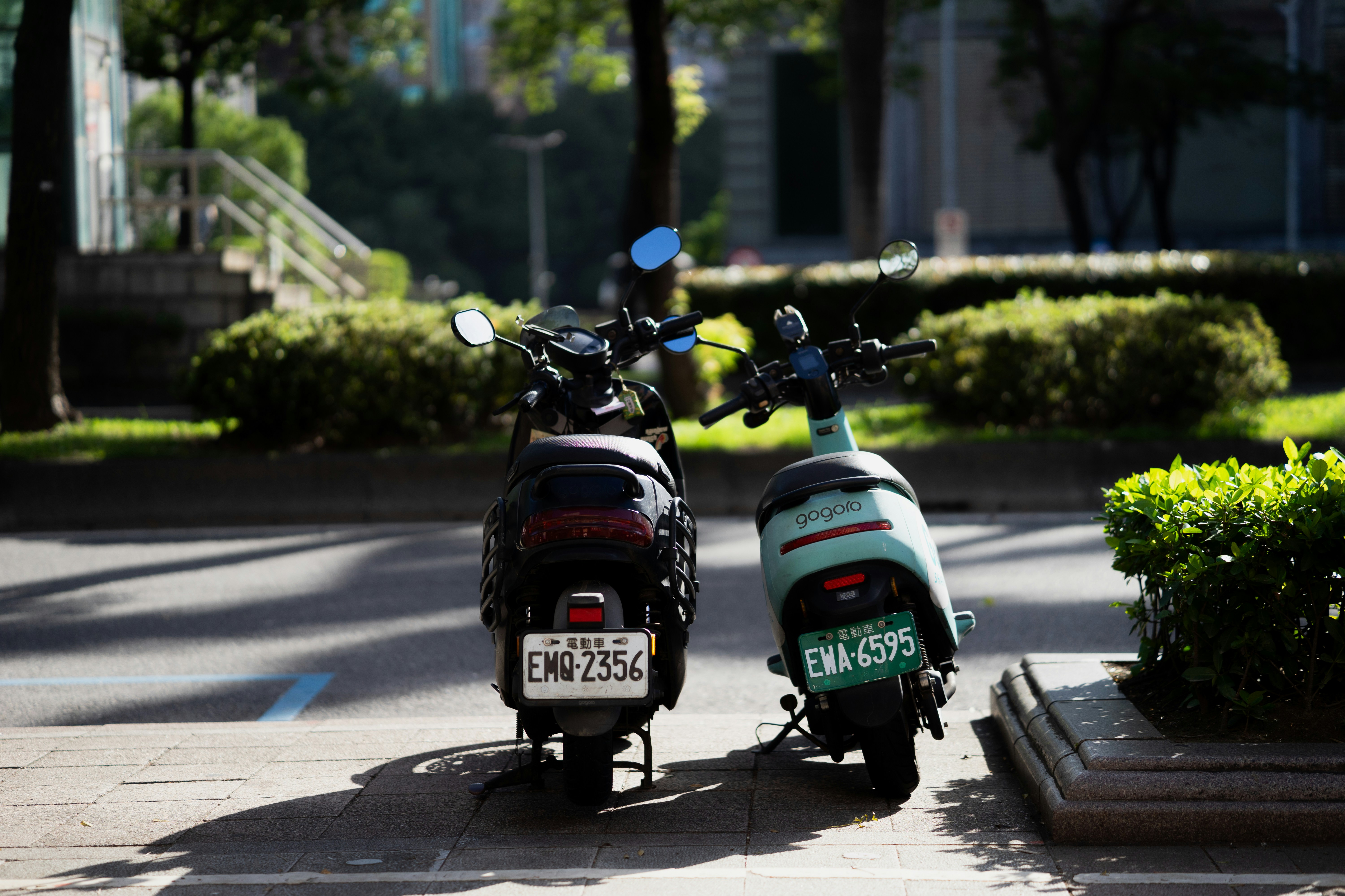 Two parked scooters on a sunny sidewalk.