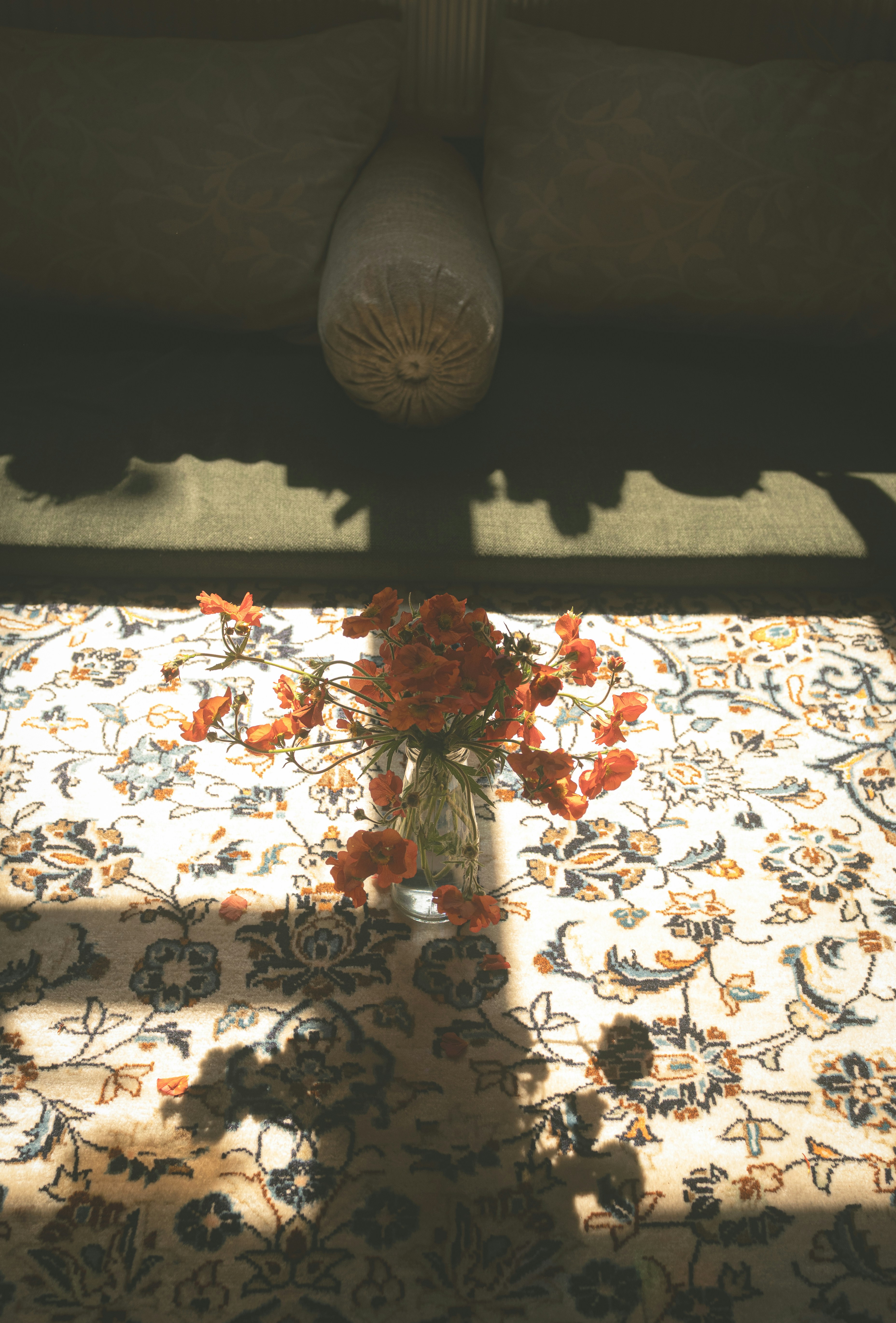 Orange flowers in a vase on a patterned rug.