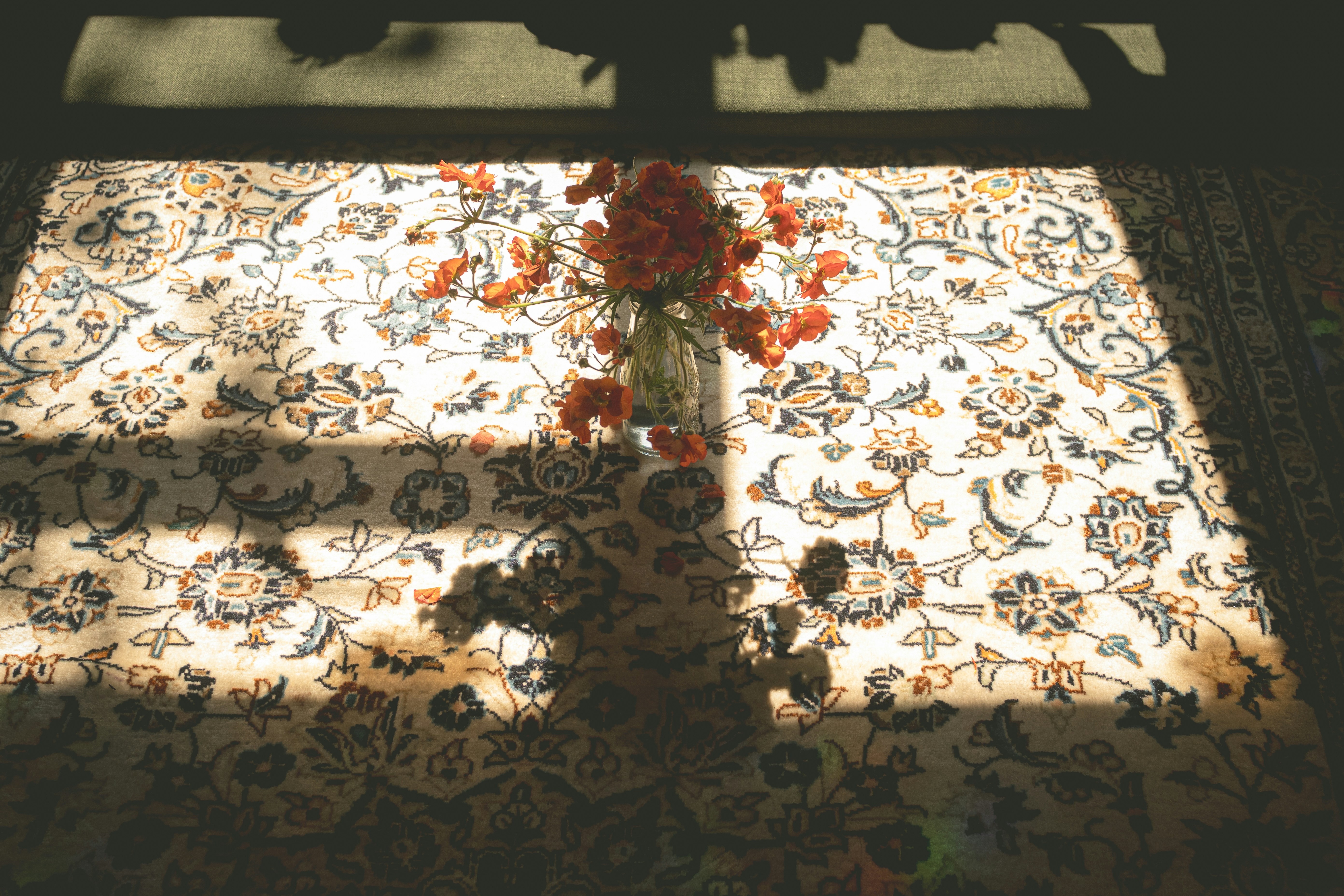 Vase of flowers on a patterned rug with sunlight.
