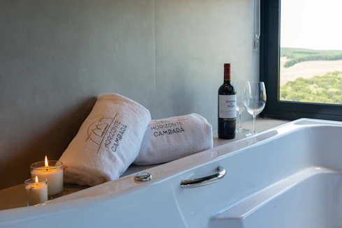 Two towels, wine bottle, and glasses by bathtub.