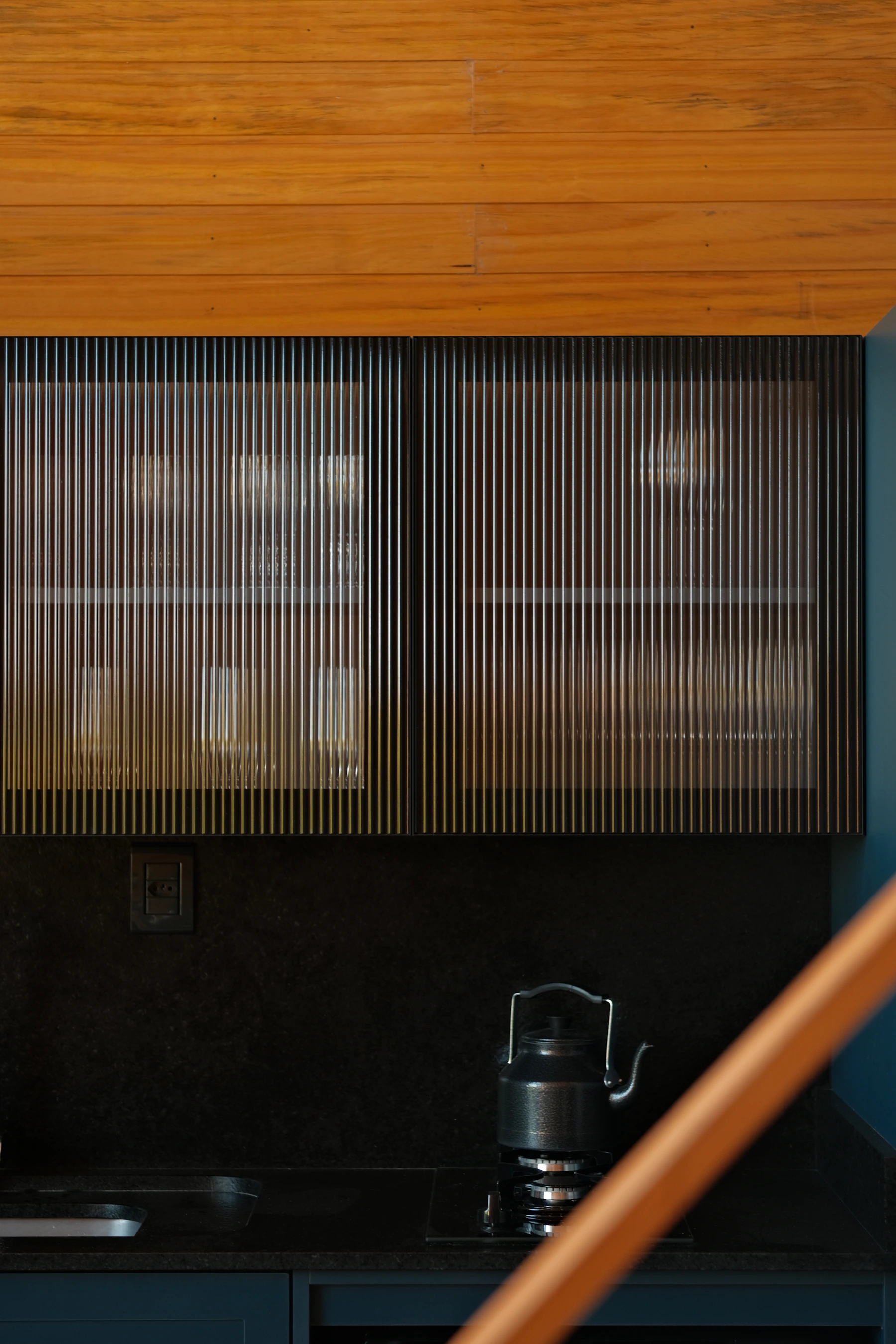 Dark kitchen wall cabinets with vertically reeded glass, partially visible dishes and a kettle below
