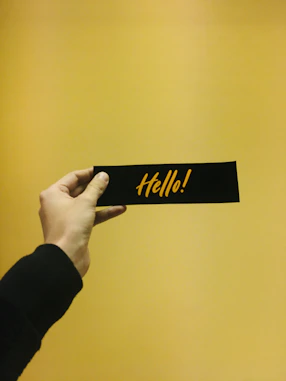 Hand holding a black strip with "hello!" written on it.