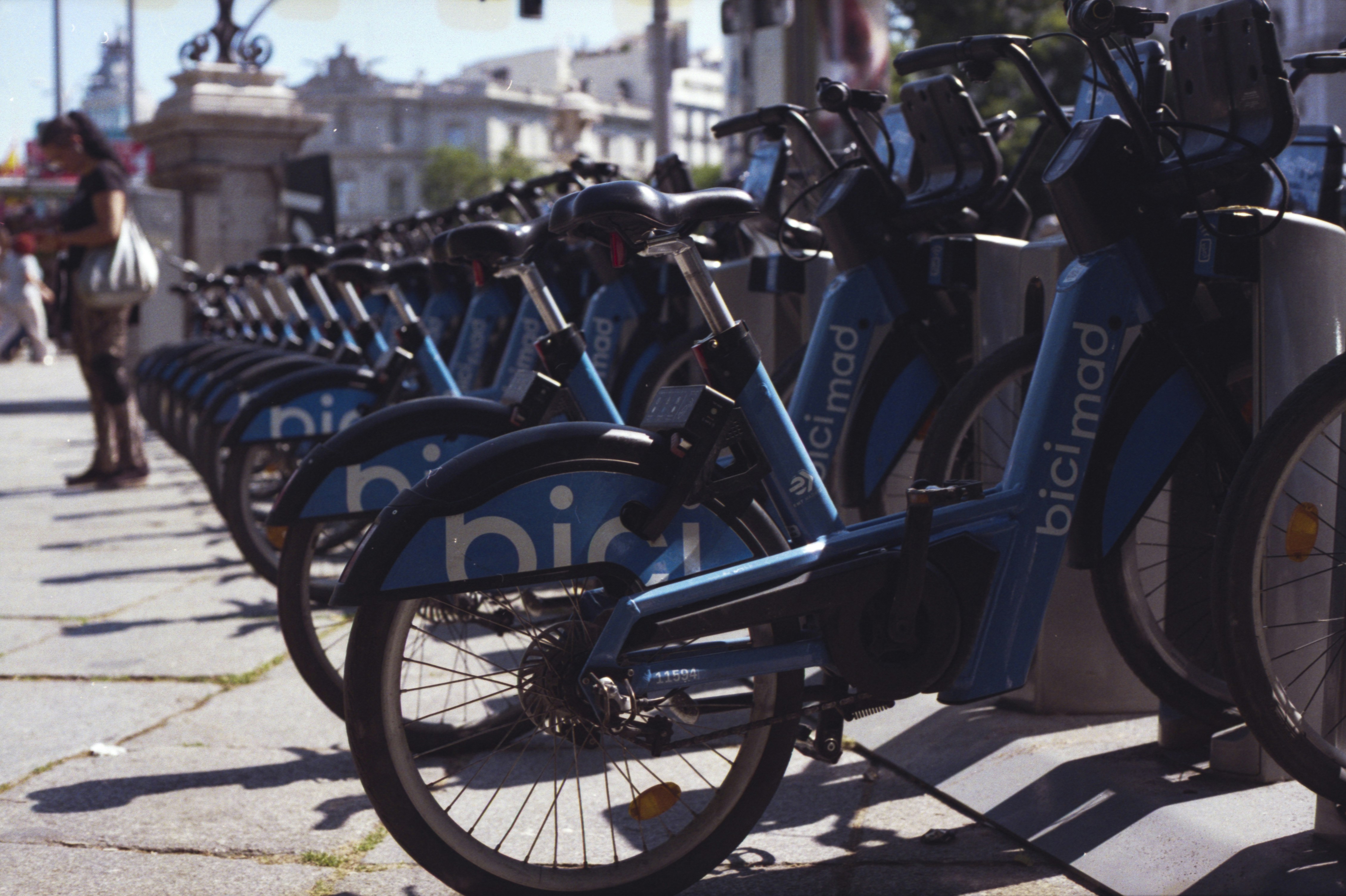 Row of blue rental bicycles parked on a sunny street.