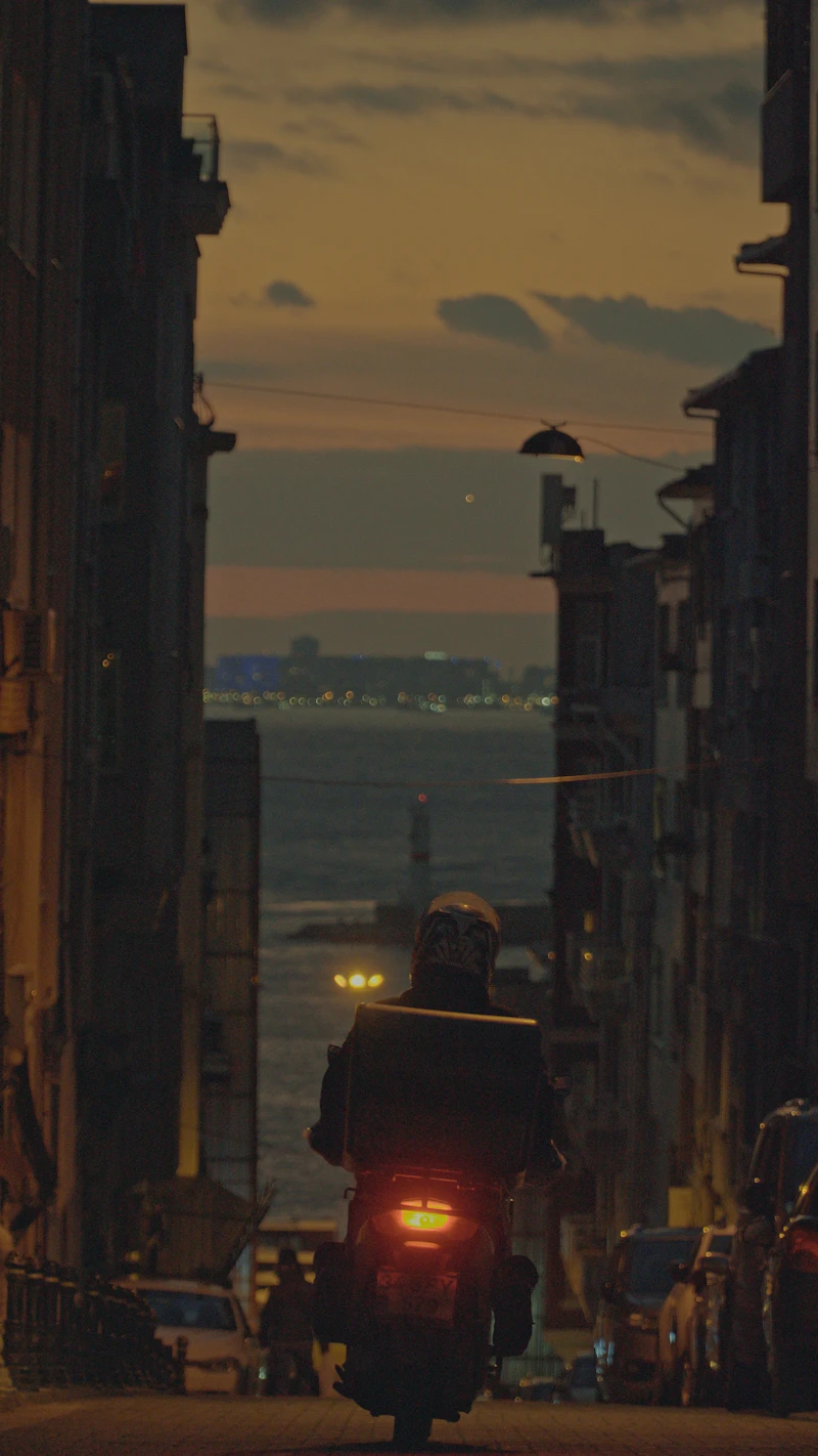 Delivery motorcyclist silhouetted against a golden dusk sky in Istanbul