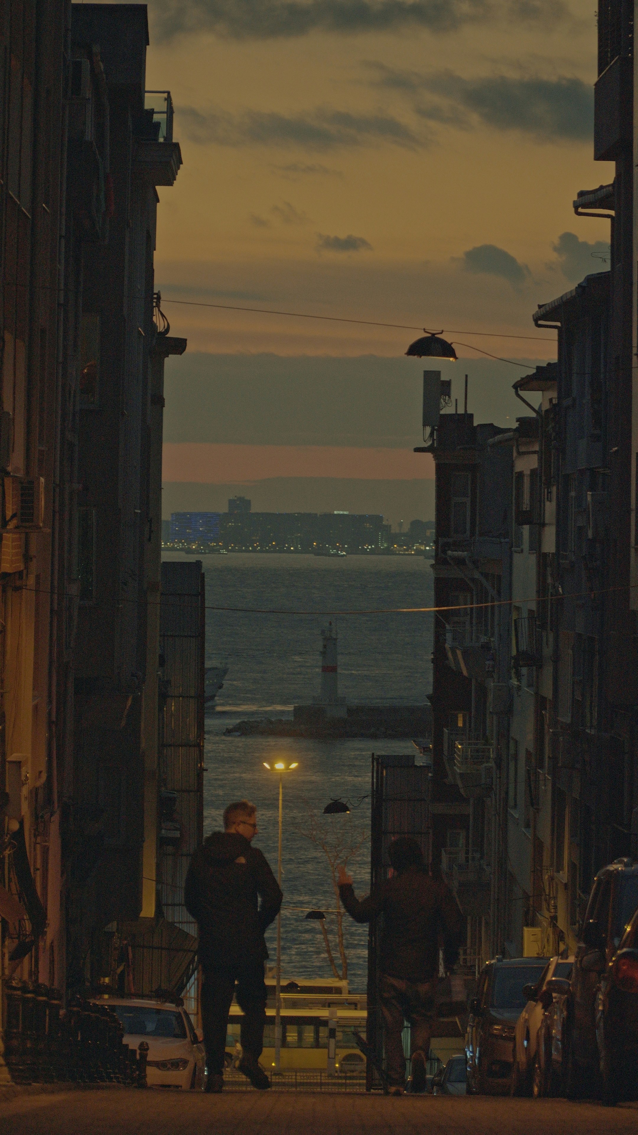 Two people walk down a street towards the sea.