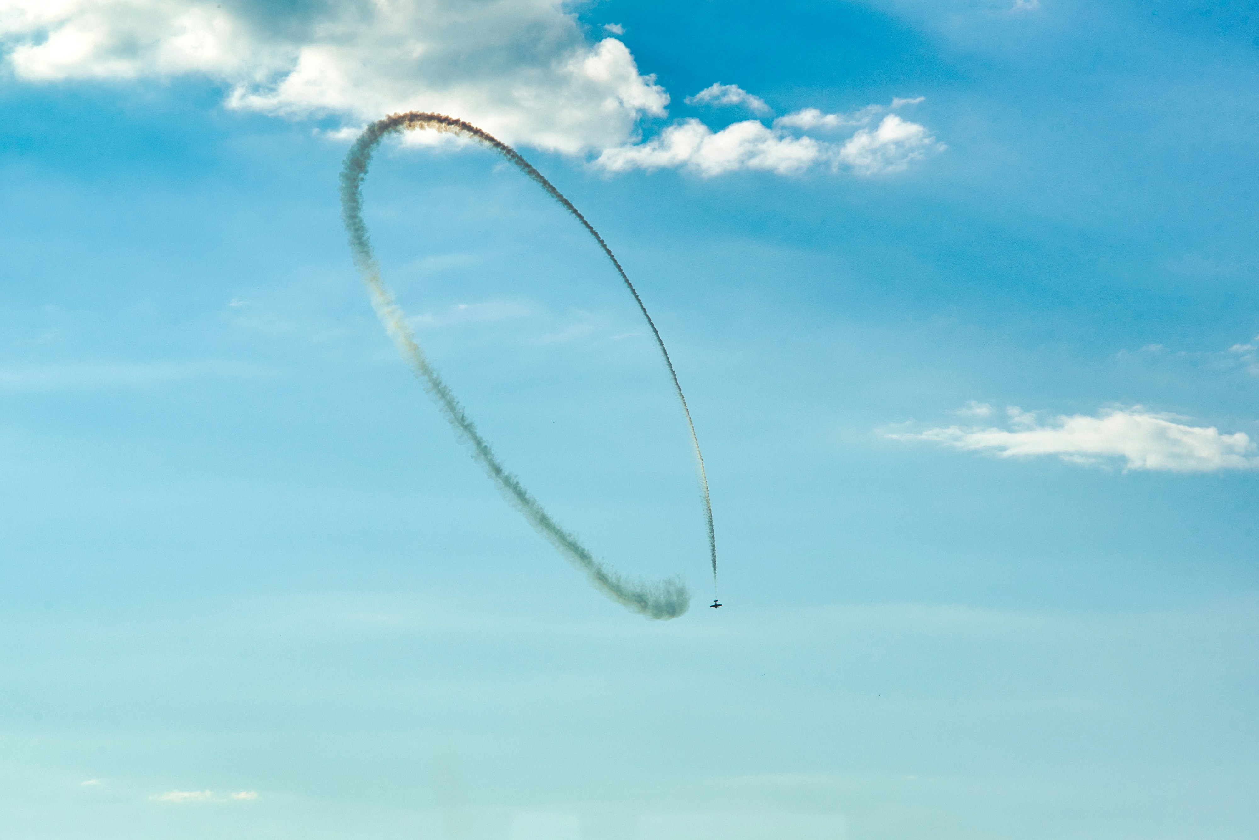 Un avión dibuja un anillo de humo en el cielo azul.