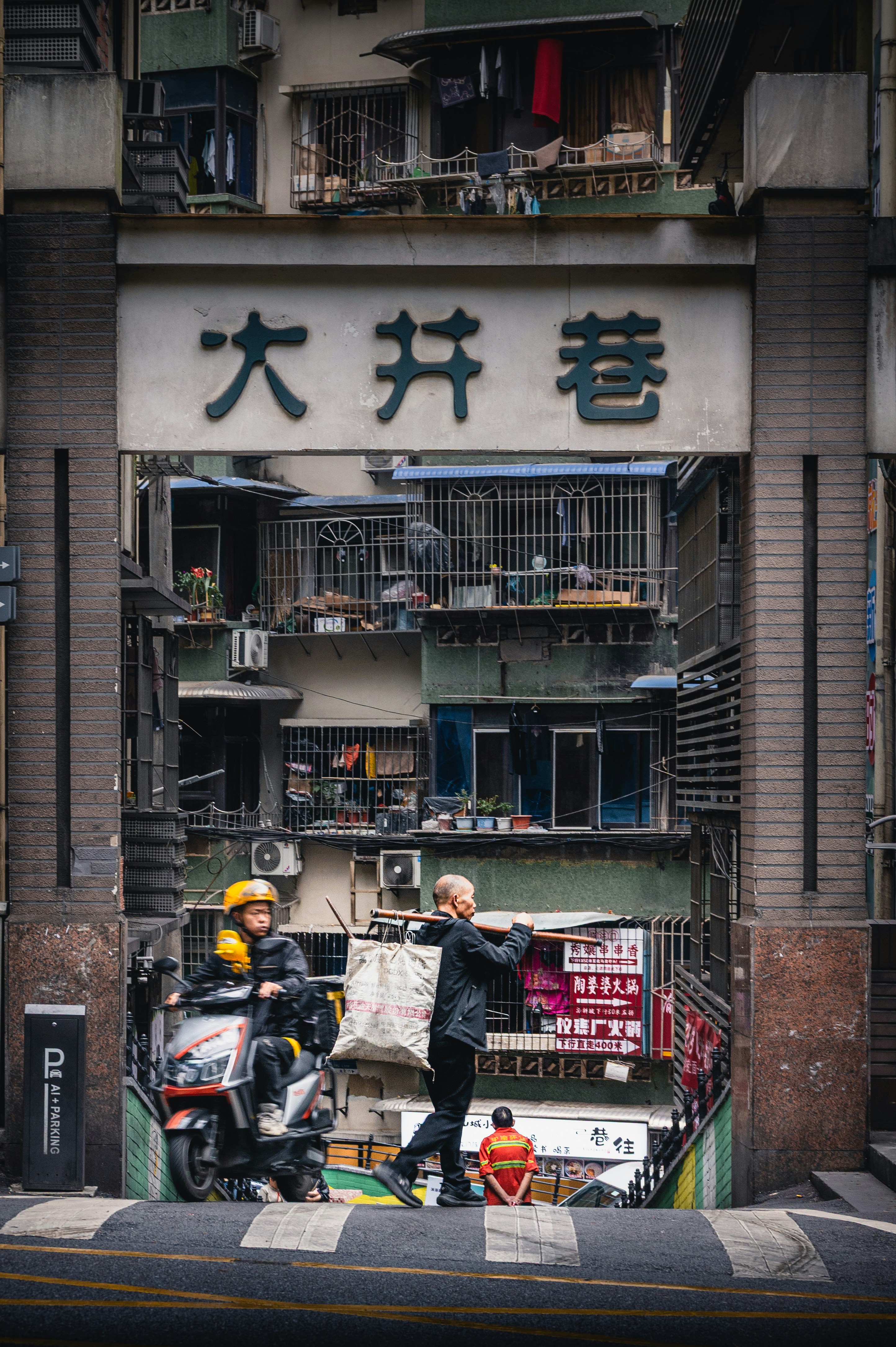 People and scooter pass through old apartment building entrance.