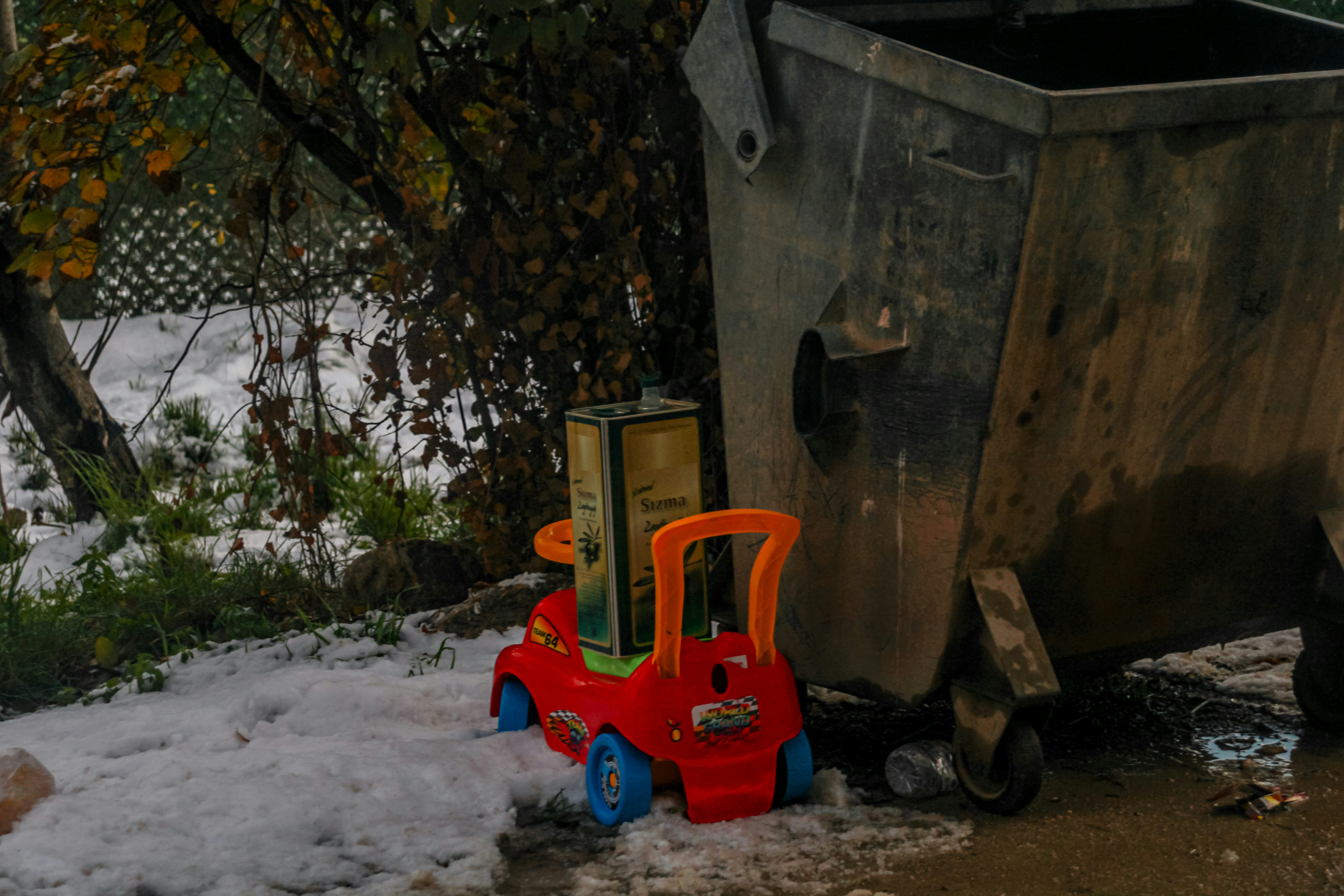 A toy car with a box beside a dumpster.