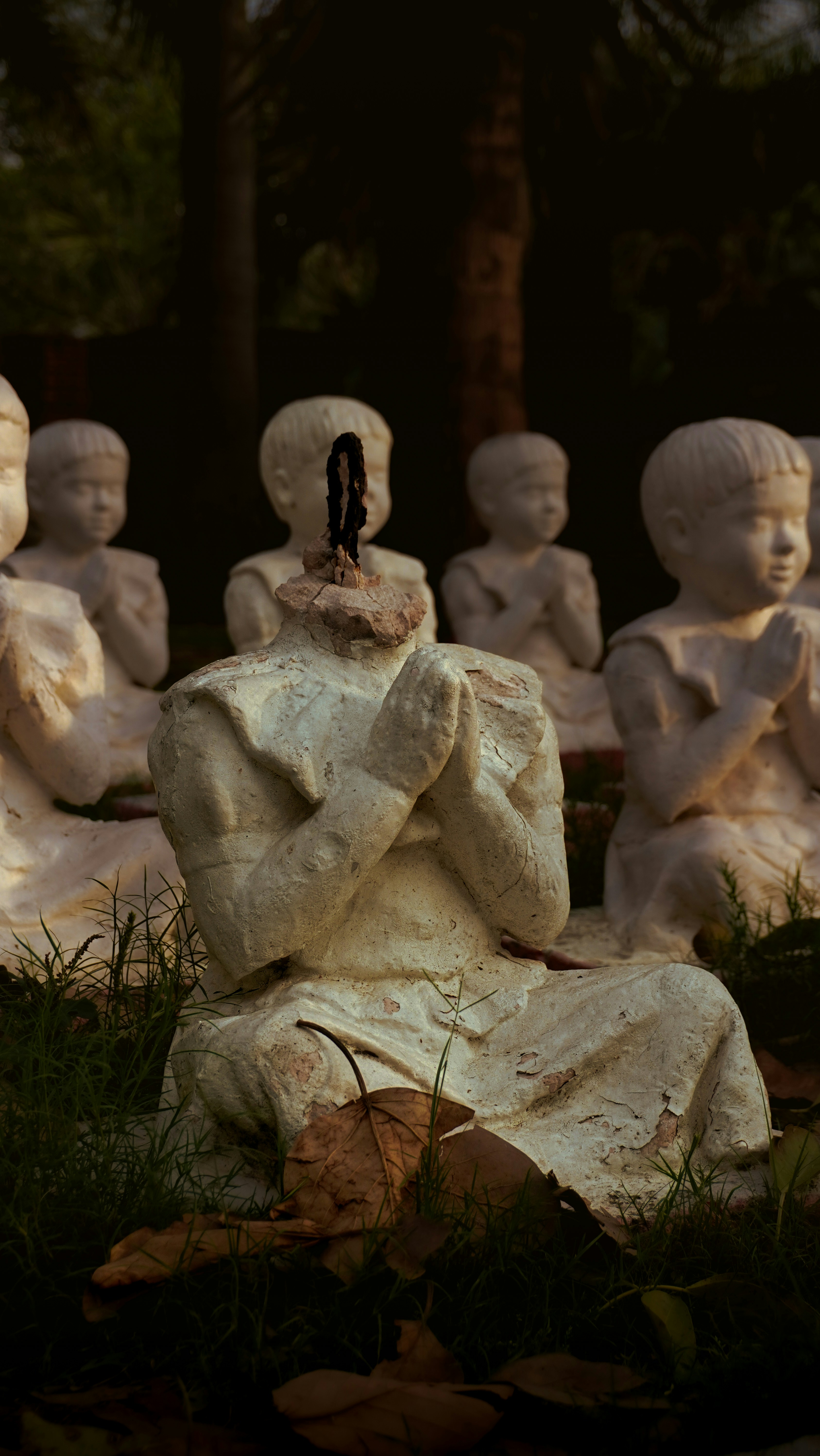 Damaged statues of children praying in a garden.