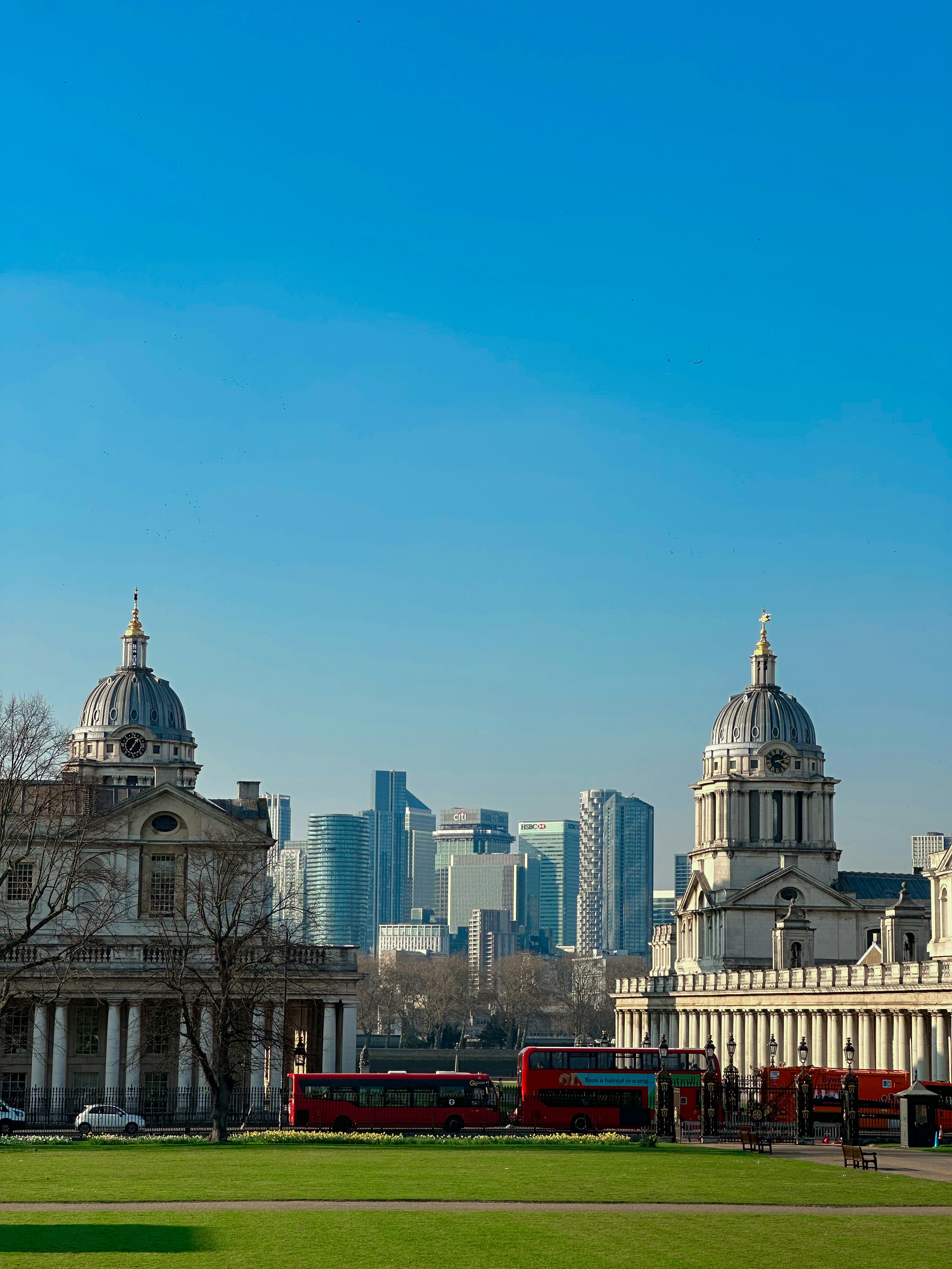 Two red double-decker buses in front of historic buildings.